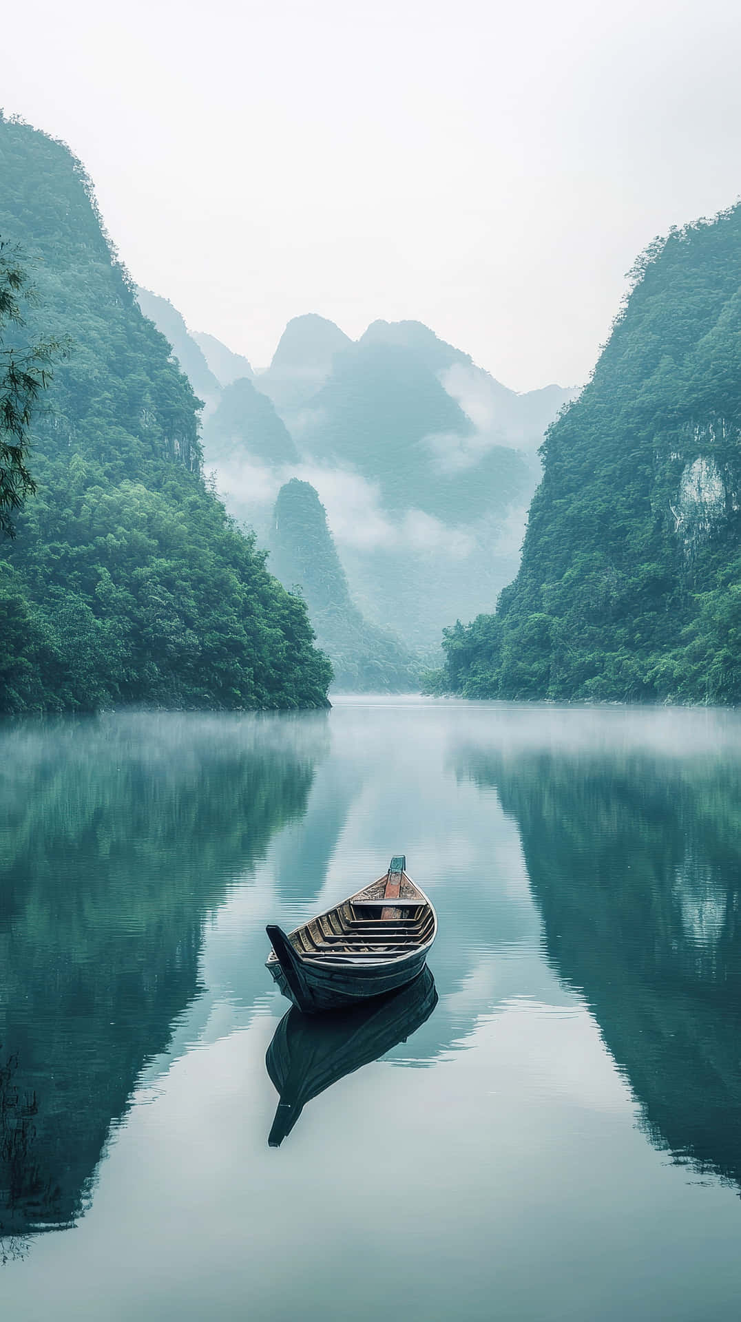 一艘小木船在平靜的水面上休息，背景是霧濛濛的山脈和茂密的綠植。