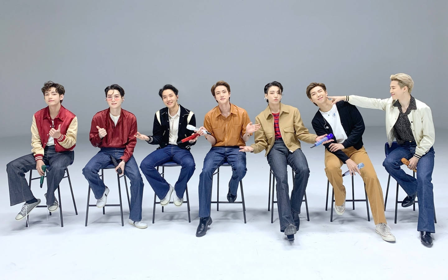 七位年輕男子身穿外套和牛仔褲坐在攝影棚的凳子上。
