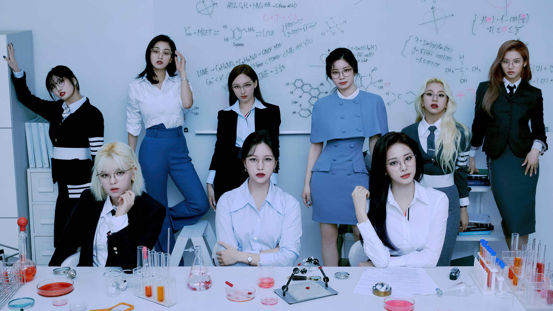 Twice 4K 愛的公式實驗室 壁紙 — 七位身穿實驗室服裝的女性自信地圍繞著一張放有燒杯和寫滿方程式的白板的科學桌擺姿勢。