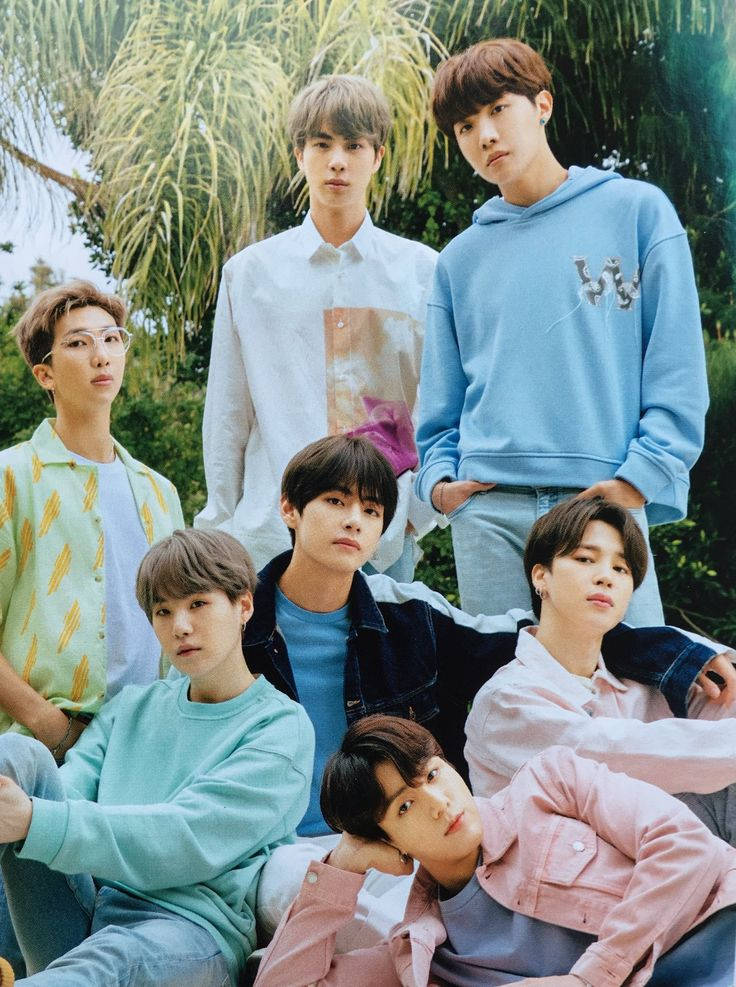 BTS戶外自然風合照 壁紙 — 七位身穿柔和色調休閒服的年輕男子在明亮的日光下，自信地站在茂密的綠色棕櫚樹中擺姿勢。