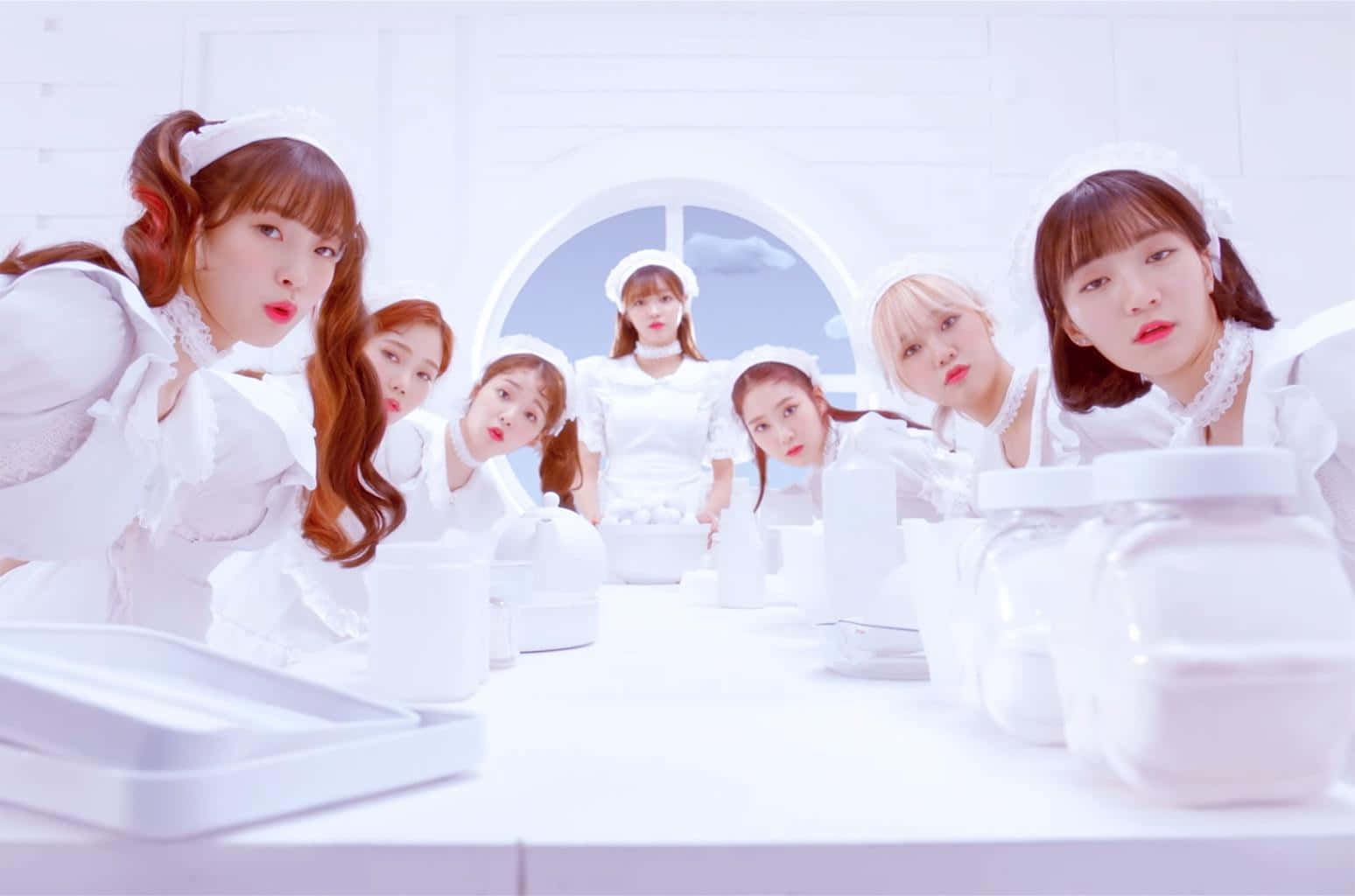 七位K-pop偶像身穿女僕裝，在白色攝影棚中俏皮地擺姿勢。