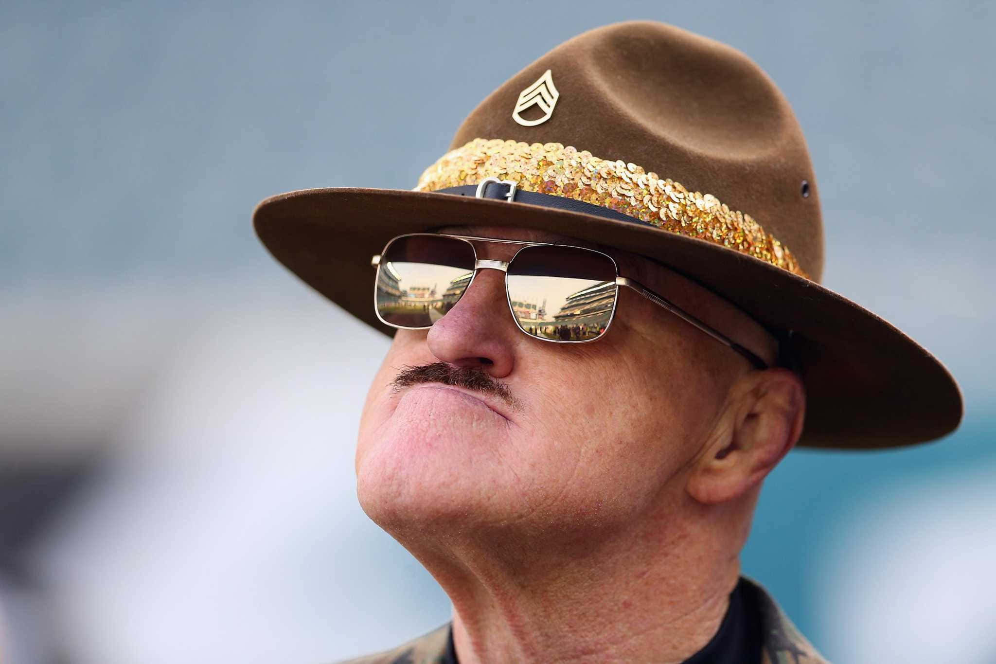 Sgt Slaughter 美國職業摔角手 壁紙 — 一個戴著金色邊緣棕色帽子和太陽眼鏡的男人，在柔和的藍天下向上看。