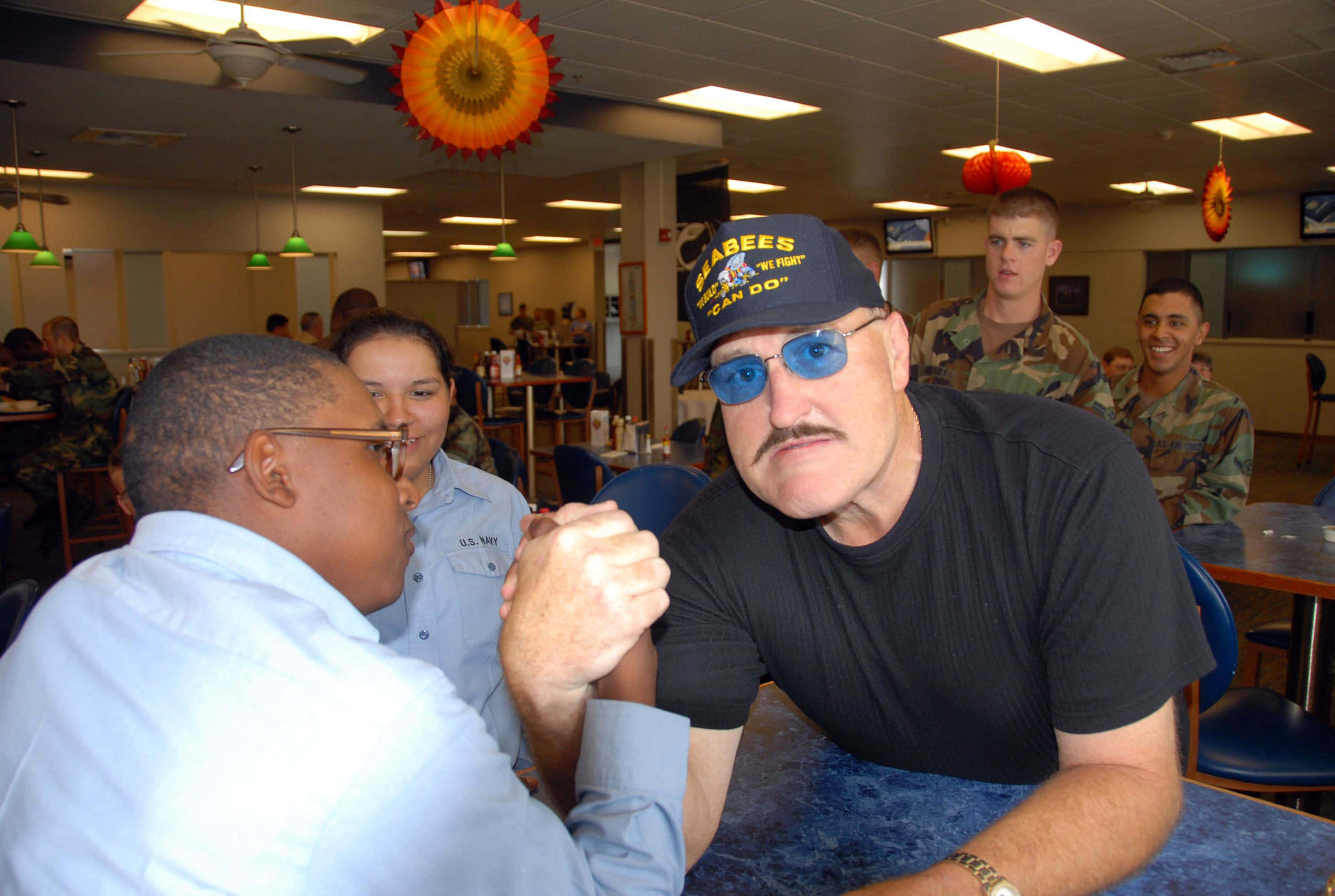 Sgt Slaughter與Lars Triggs進行掰手腕 壁紙 — 兩名男子在軍人食堂進行腕力比賽，其他軍人在旁觀看。
