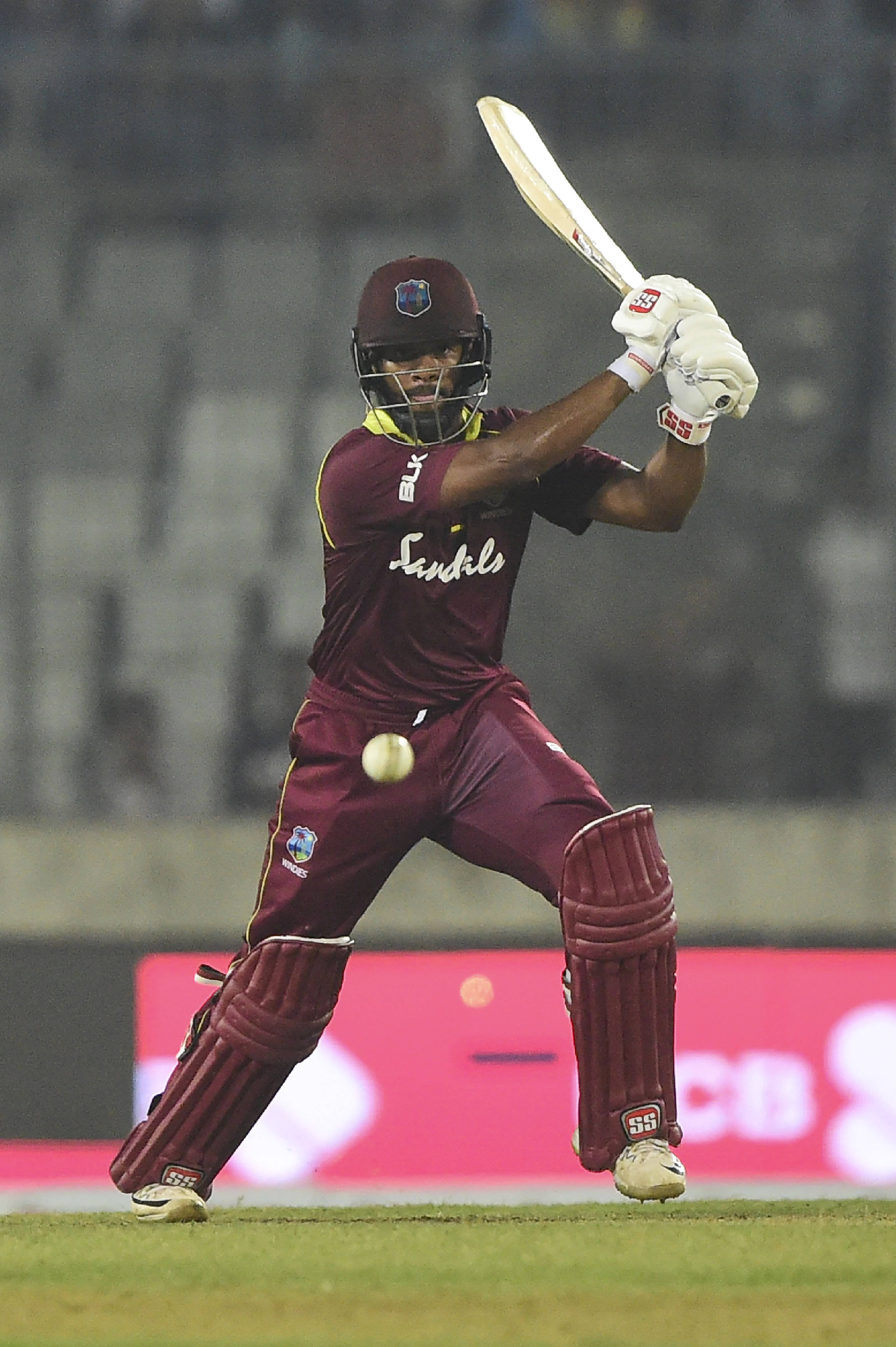Shai Hope 握球棒 壁紙 — 一名身穿棗紅色球衣的板球擊球手在夜間比賽中，在球場燈光下揮動球棒擊球。