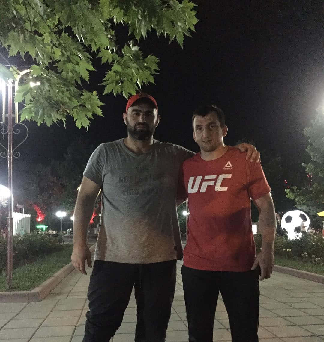 兩個男人在夜晚、公園裡、有照明的街燈和樹木一起站立。