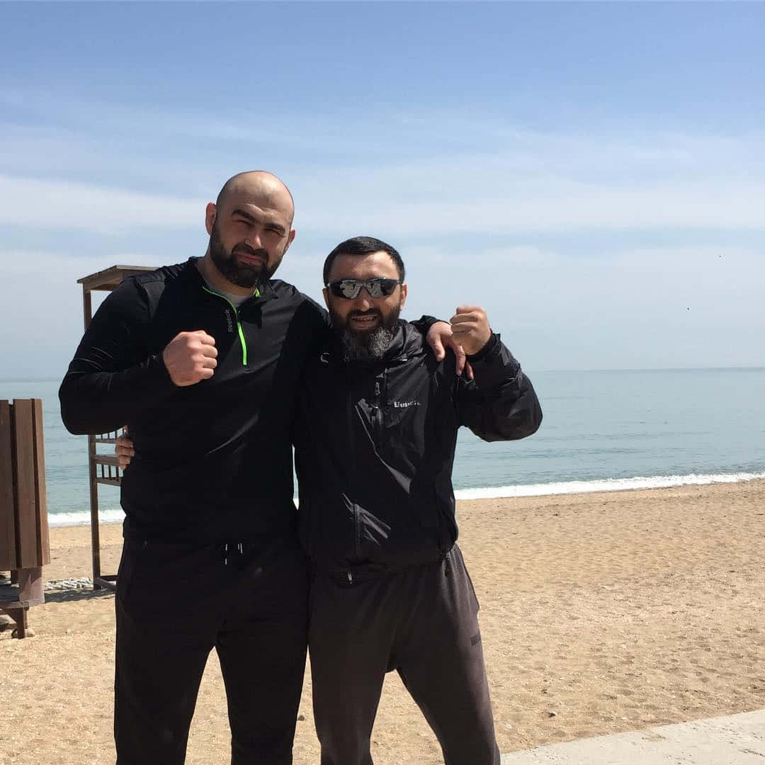 兩位身穿運動服的男士在陽光明媚的海灘上以海洋為背景擺姿勢。