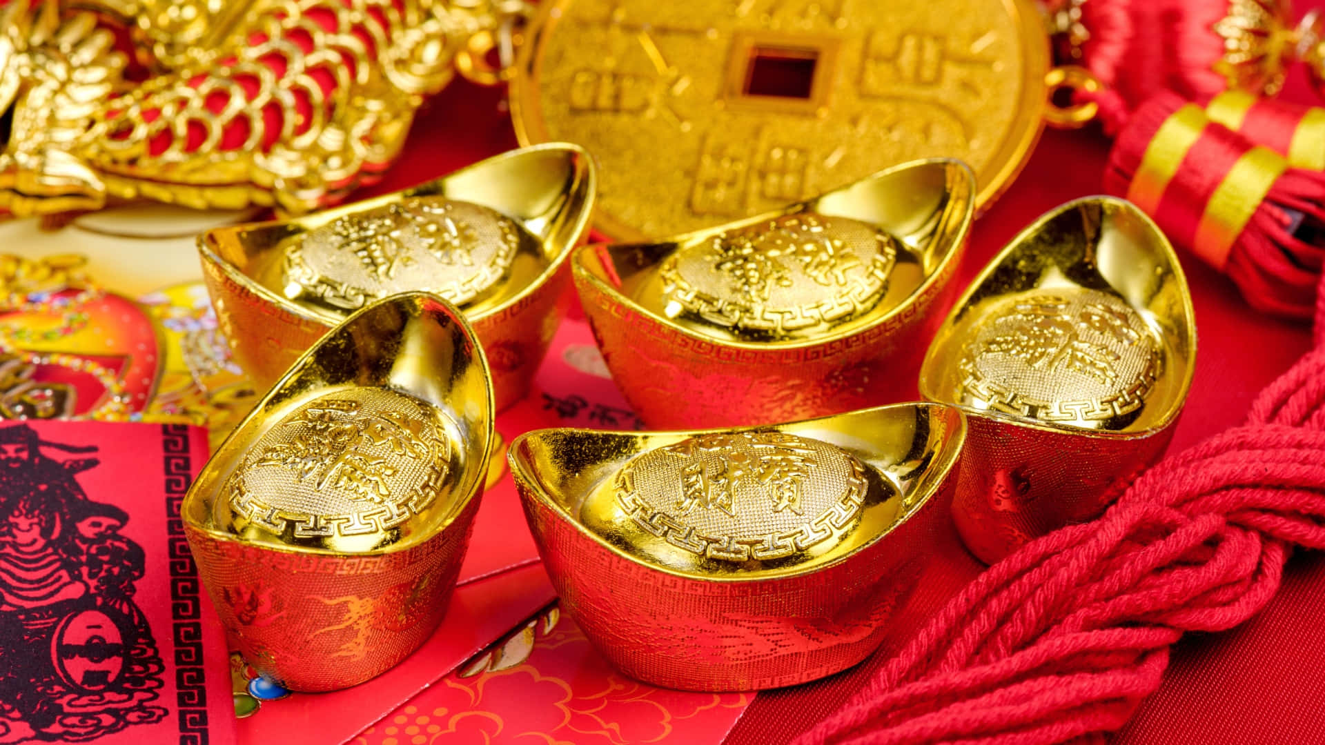  壁紙 — 閃亮的金條和金幣放在鮮紅色的紙上，並有喜慶的中國新年裝飾。