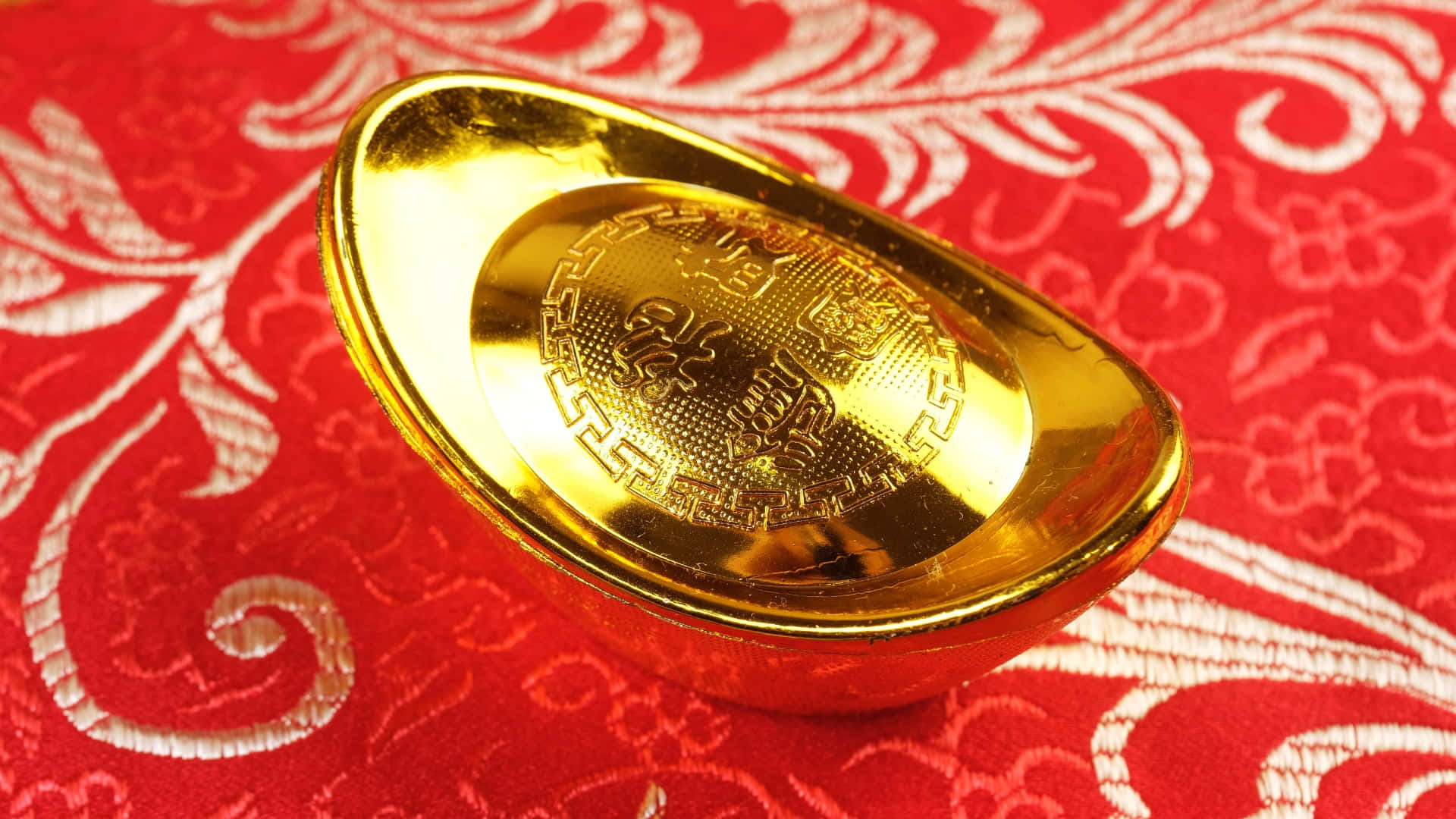  壁紙 — 閃閃發光的金條放在帶有精緻白色花卉刺繡的濃郁紅色布料上。