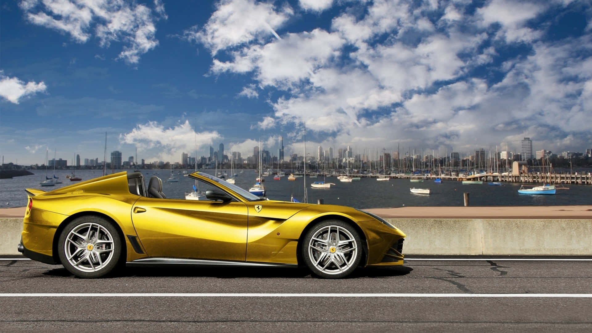 Ferrari F12 Berlinetta 桌布 壁紙 — 一輛閃閃發光的金色法拉利敞篷車沿著海濱道路行駛，背景是城市天際線和遊艇碼頭，天空湛藍，白雲朵朵。