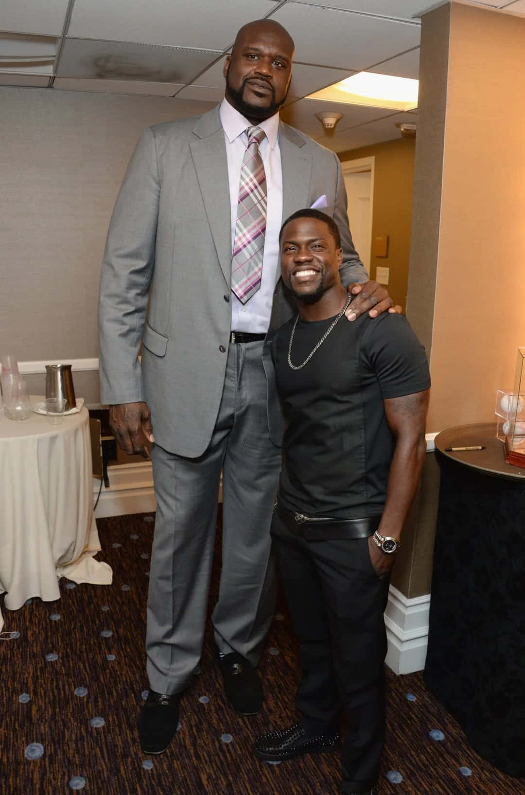  壁紙 — Shaquille O'Neal 身穿灰色西裝，在室內活動中高聳站立於身穿黑色服裝、面帶微笑的 Kevin Hart 身旁。