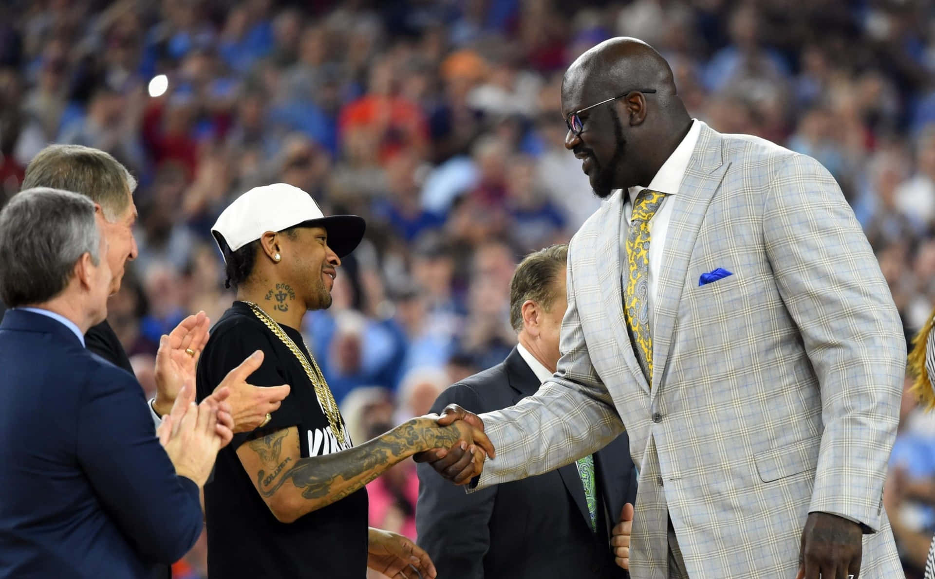  壁紙 — Shaquille O'Neal 身穿格紋西裝，在擠滿觀眾的籃球場上與一位有紋身的運動員握手。