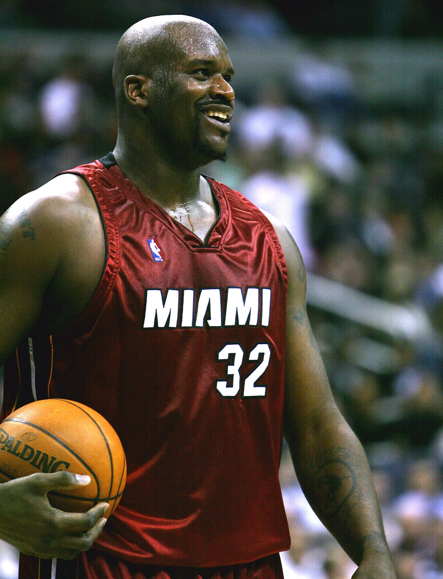  壁紙 — Shaquille O'Neal 身穿紅色邁阿密球衣，在比賽中微笑著抱著籃球，背景是模糊的人群。