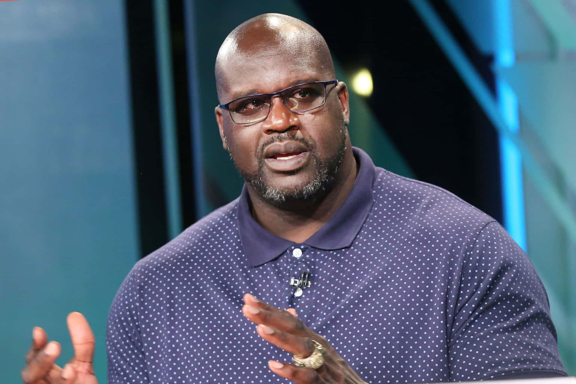  壁紙 — Shaquille O'Neal 在錄影室中穿著波點襯衫和眼鏡，一邊說話一邊做手勢。