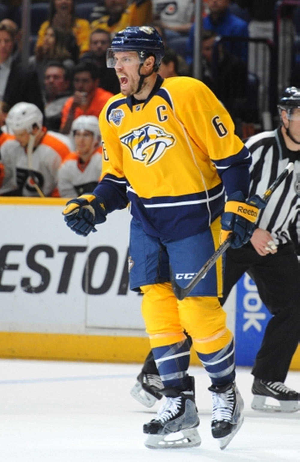 Shea Weber 炫耀納什維爾掠奪者隊球衣 壁紙 — 一位穿著黃色和藍色裝備的納什維爾掠奪者冰球球員在比賽中，在裁判附近激情地在冰上大喊。