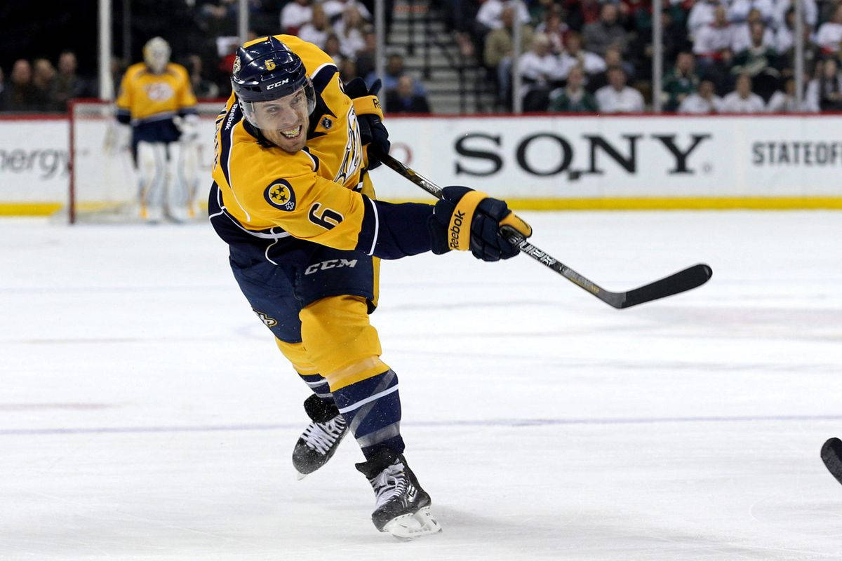 Shea Weber 穿納什維爾掠奪者隊球衣海報 壁紙 — 一名身穿黃色和深藍色裝備的冰球運動員在比賽中專注地在冰上動態滑行。