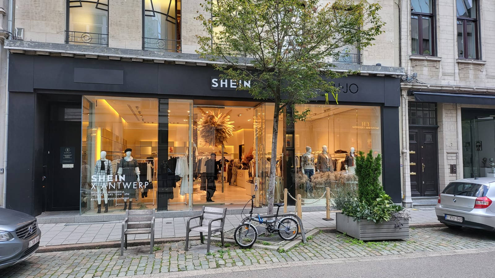 SHEIN時裝店正面，夜間鵝卵石行人路上有人體模型和單車。