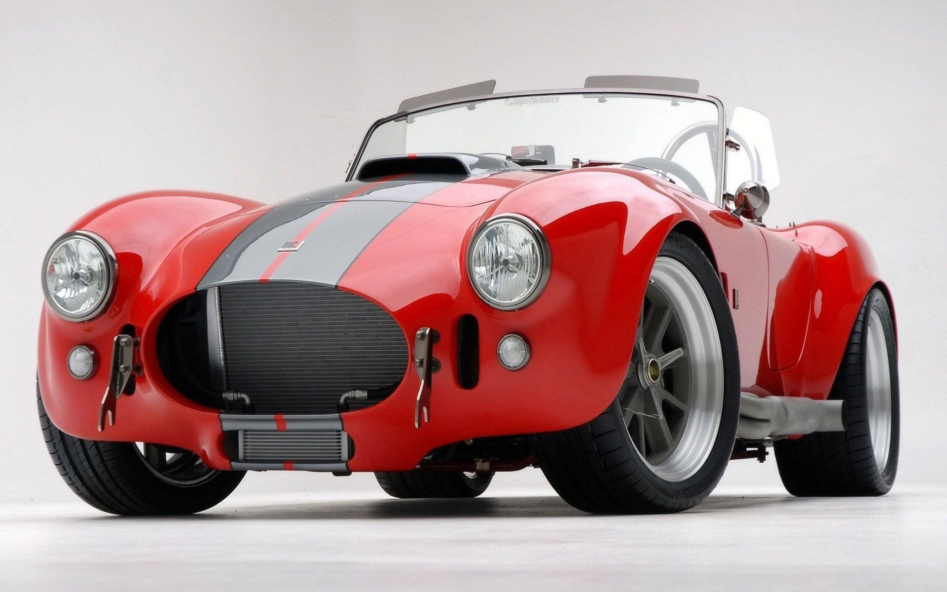 Shelby iPhone Cobra款 壁紙 — 一輛光澤的紅色經典跑車，帶有黑色賽車條紋和鍍鉻裝飾，在純白色工作室背景前矗立。