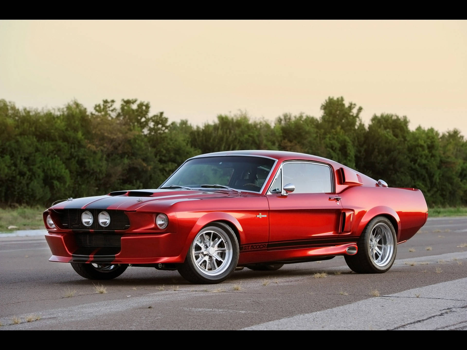 Shelby iPhone GT 500 CR模型 壁紙 — 一輛光澤的紅色經典肌肉車，帶有黑色賽車條紋，在黃金時段停在瀝青路上。