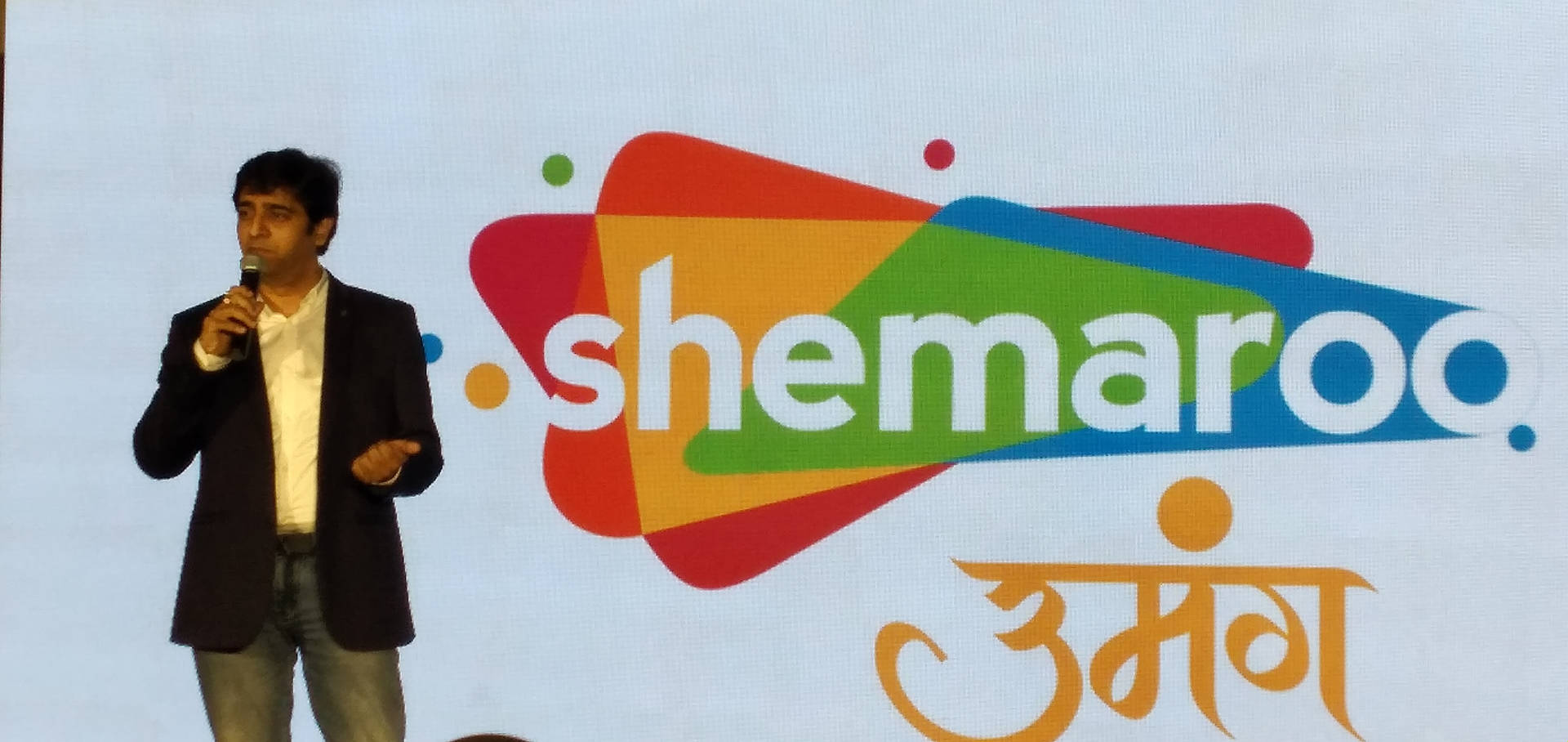 男子在舞台上進行演示，身後有Shemaroo標誌。
