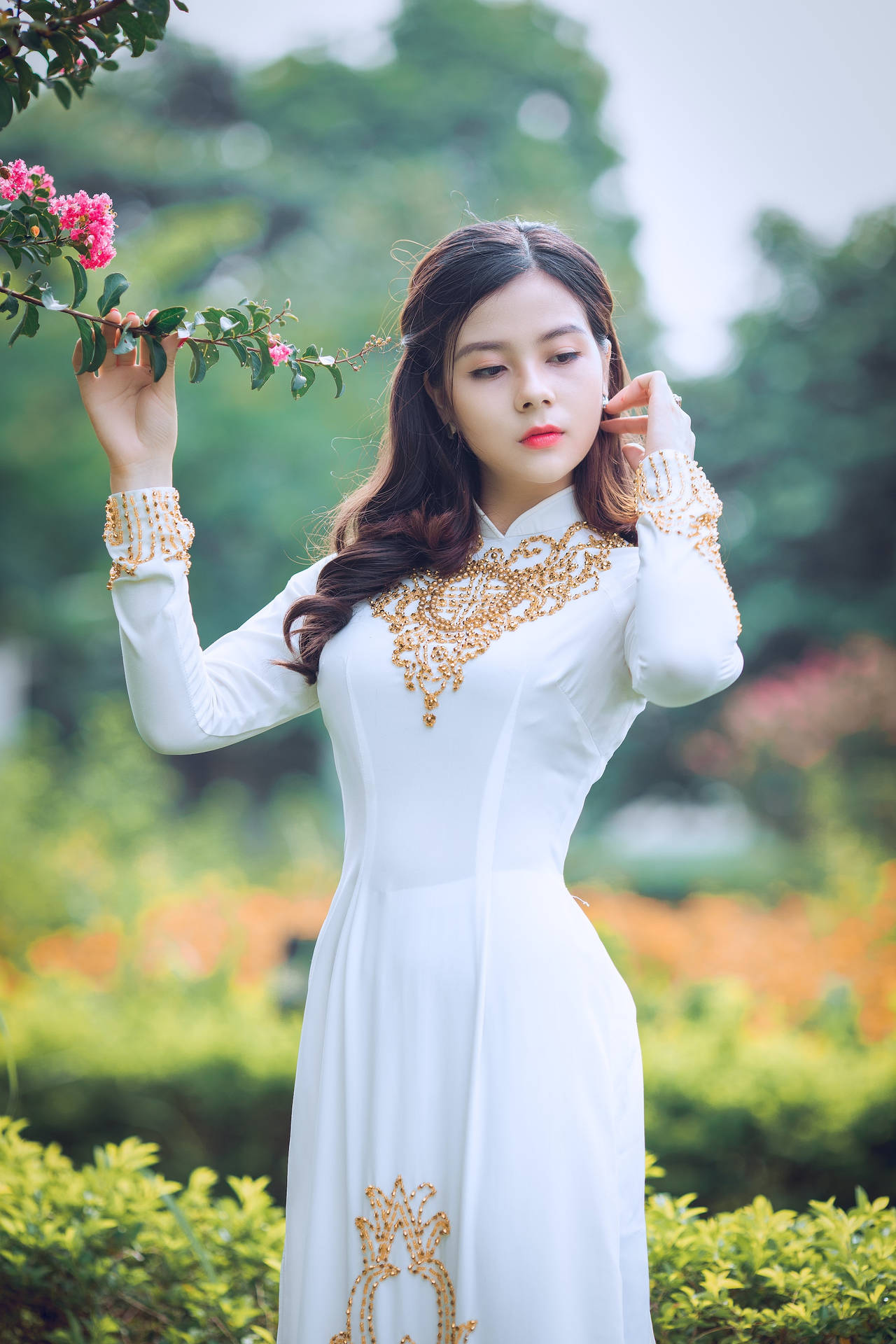身穿白色刺繡裙的女子在花園中手持粉紅花朵