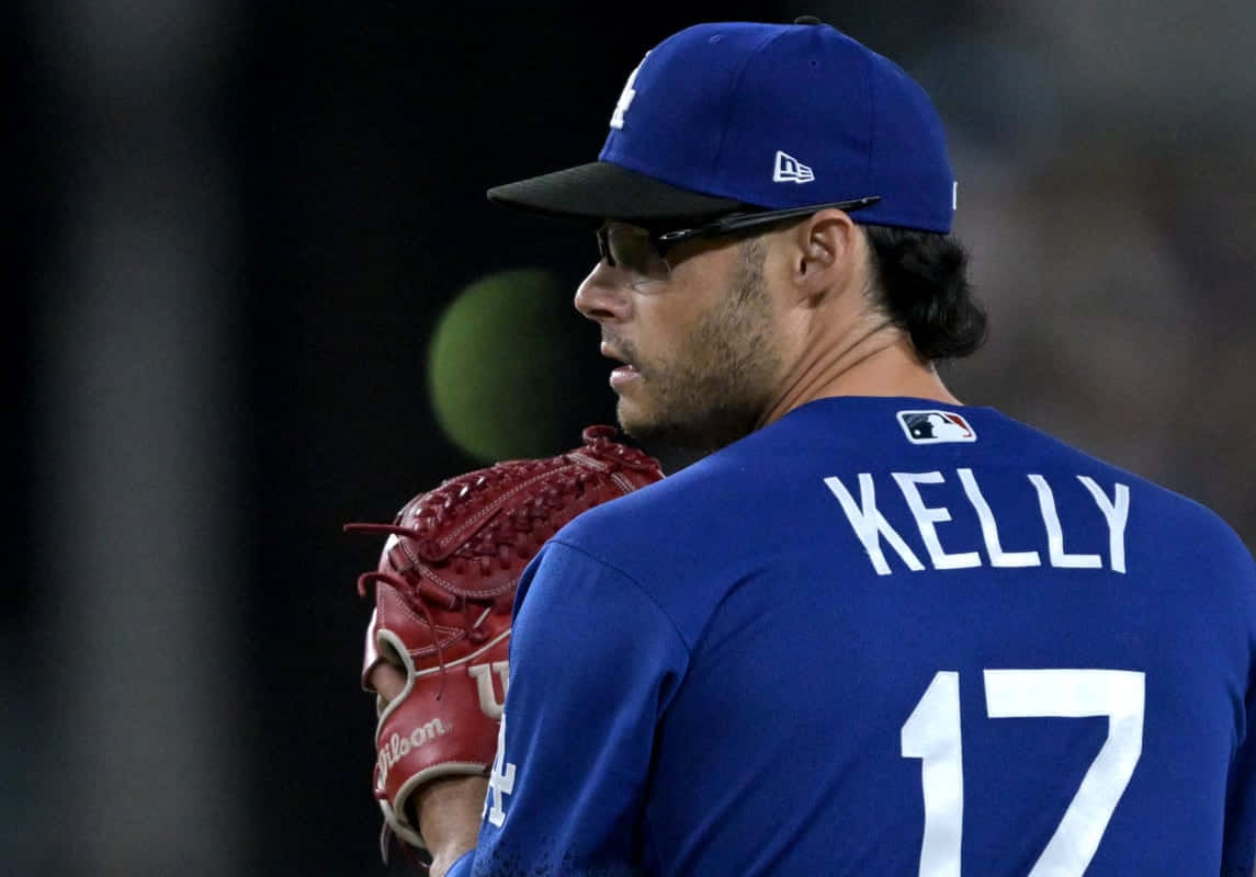  壁紙 — 身穿藍色制服和紅色手套的棒球選手Kelly在體育場燈光下的夜間比賽中專注地站立。