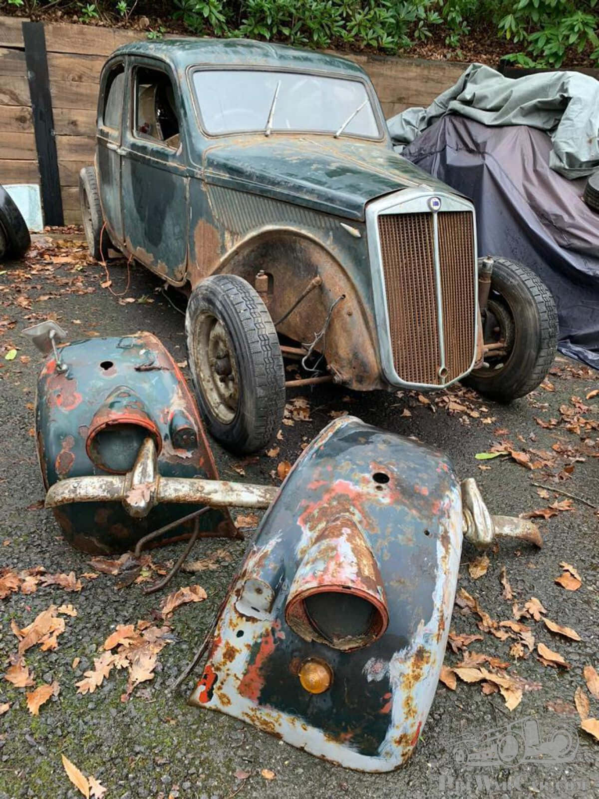  壁紙 — 一架生鏽的經典汽車被遺棄在散落著落葉的碎石地上，擋泥板已脫落。