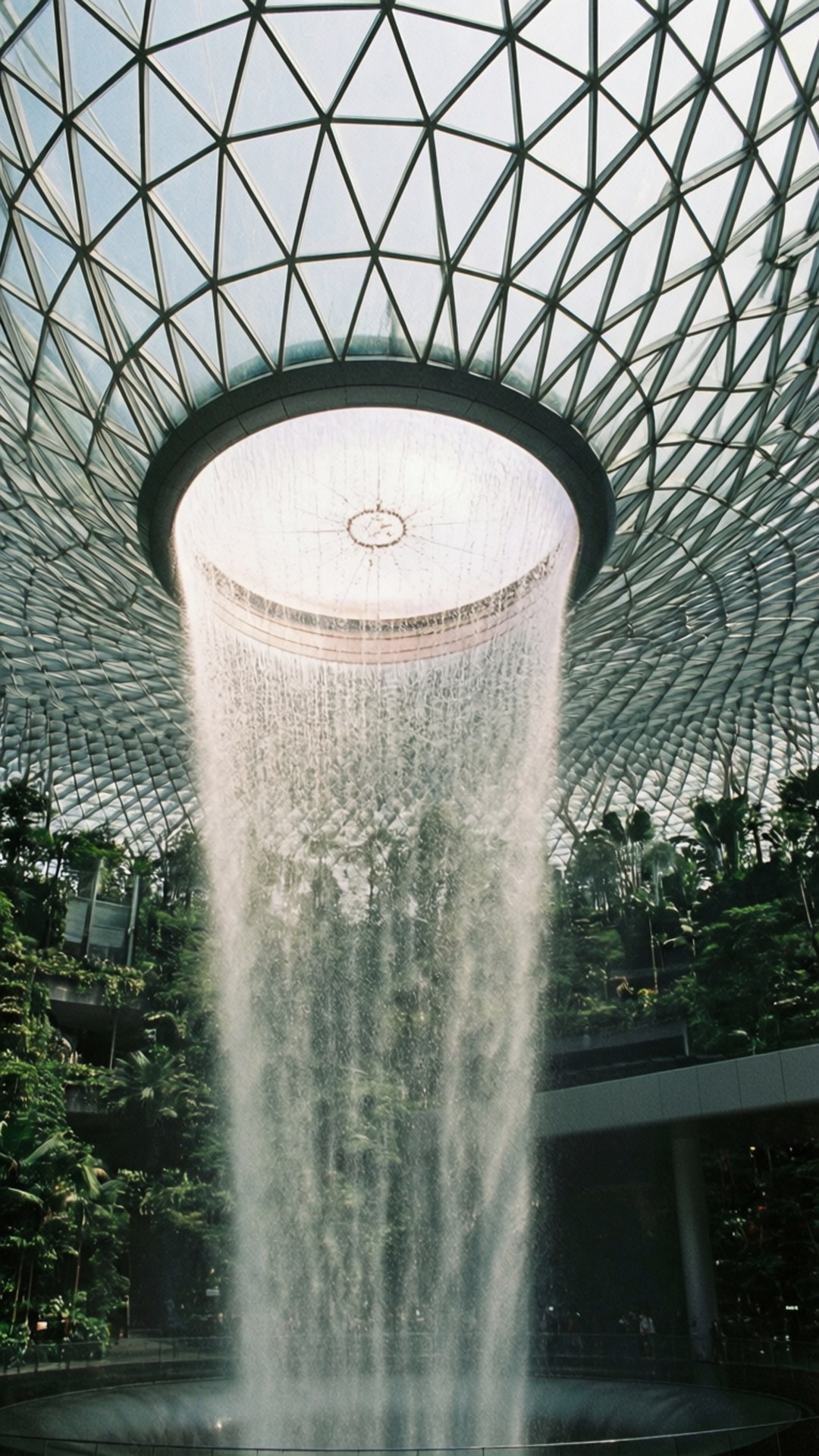 Singapore 桌布 壁紙 — 一個巨大的室內瀑布從幾何玻璃穹頂下的圓形開口傾瀉而下，周圍環繞著茂密的綠色植物。