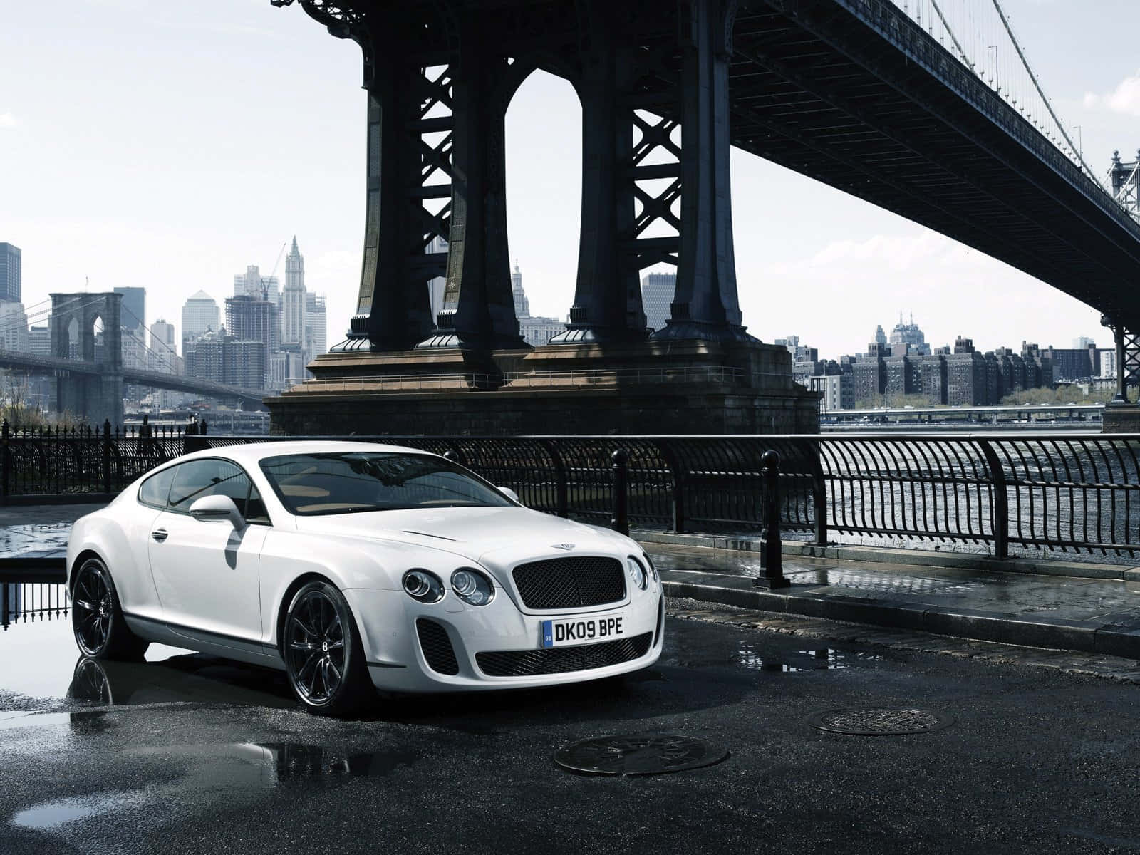 Bentley Continental Gt 桌布 壁紙 — 一架時尚的白色賓利 Continental GT 停泊在布魯克林大橋下，背景是濕漉漉的城市街道和城市天際線。