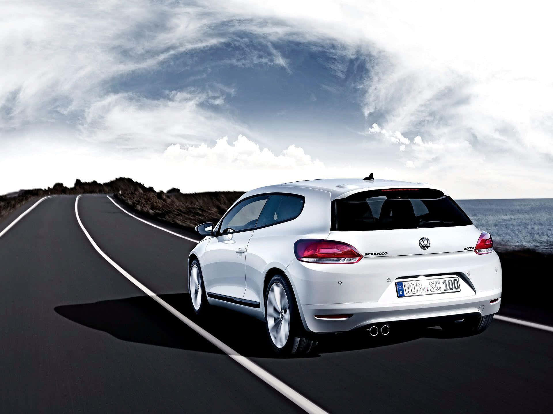 Volkswagen Scirocco 桌布 壁紙 — 一輛時尚的白色福士偉士牌Scirocco在戲劇性的多雲天空下行駛於沿海公路。