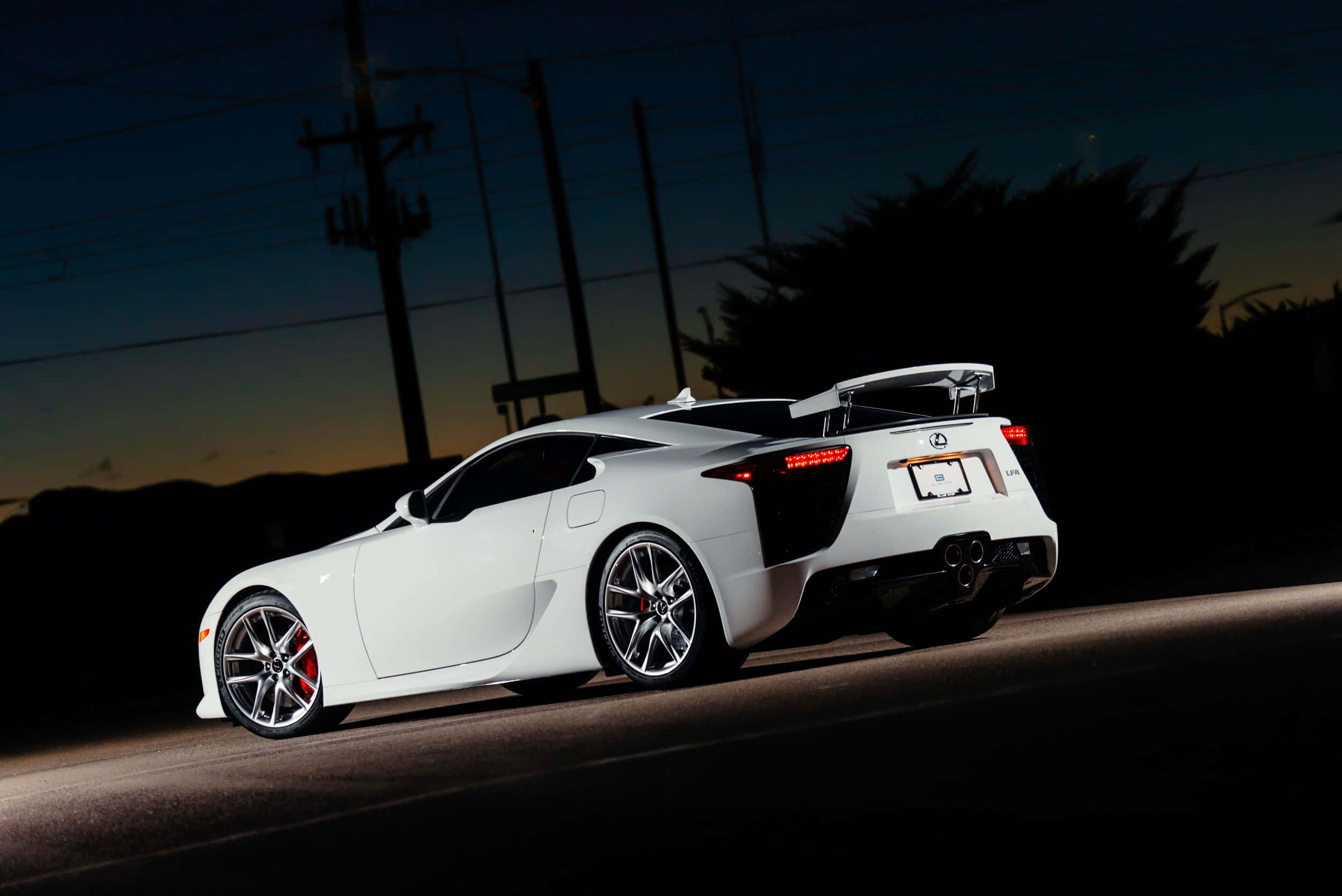 Lexus Lfa 桌布 壁紙 — 一輛時尚的白色跑車在暮色中沿著黑暗的道路行駛，發光的尾燈和輪廓分明的電線在漸暗的天空下顯得格外突出。