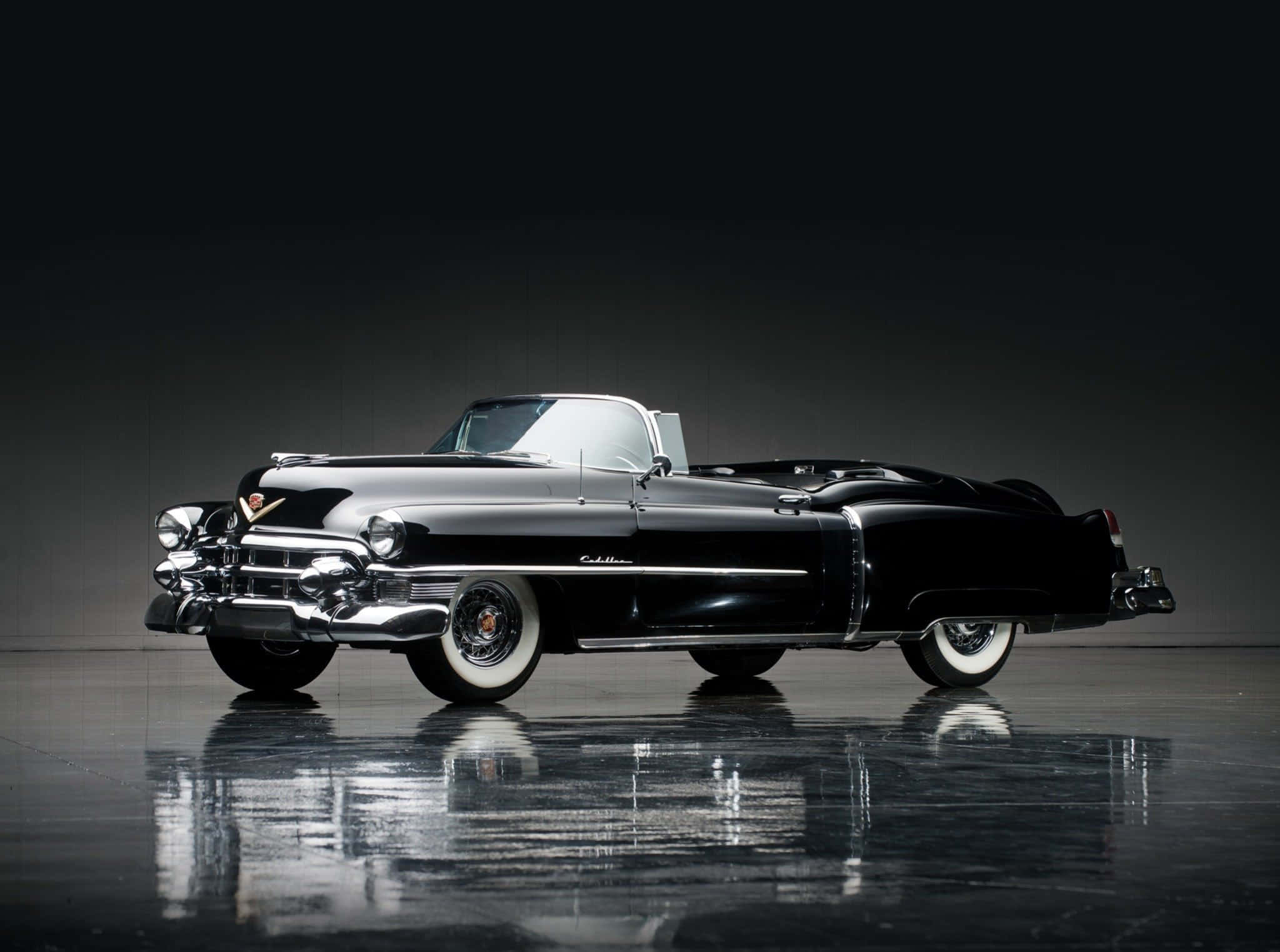 Cadillac Eldorado 桌布 壁紙 — 一輛時尚的黑色1950年代凱迪拉克敞篷車在深色背景下的反光地板上，在工作室燈光下閃閃發光。