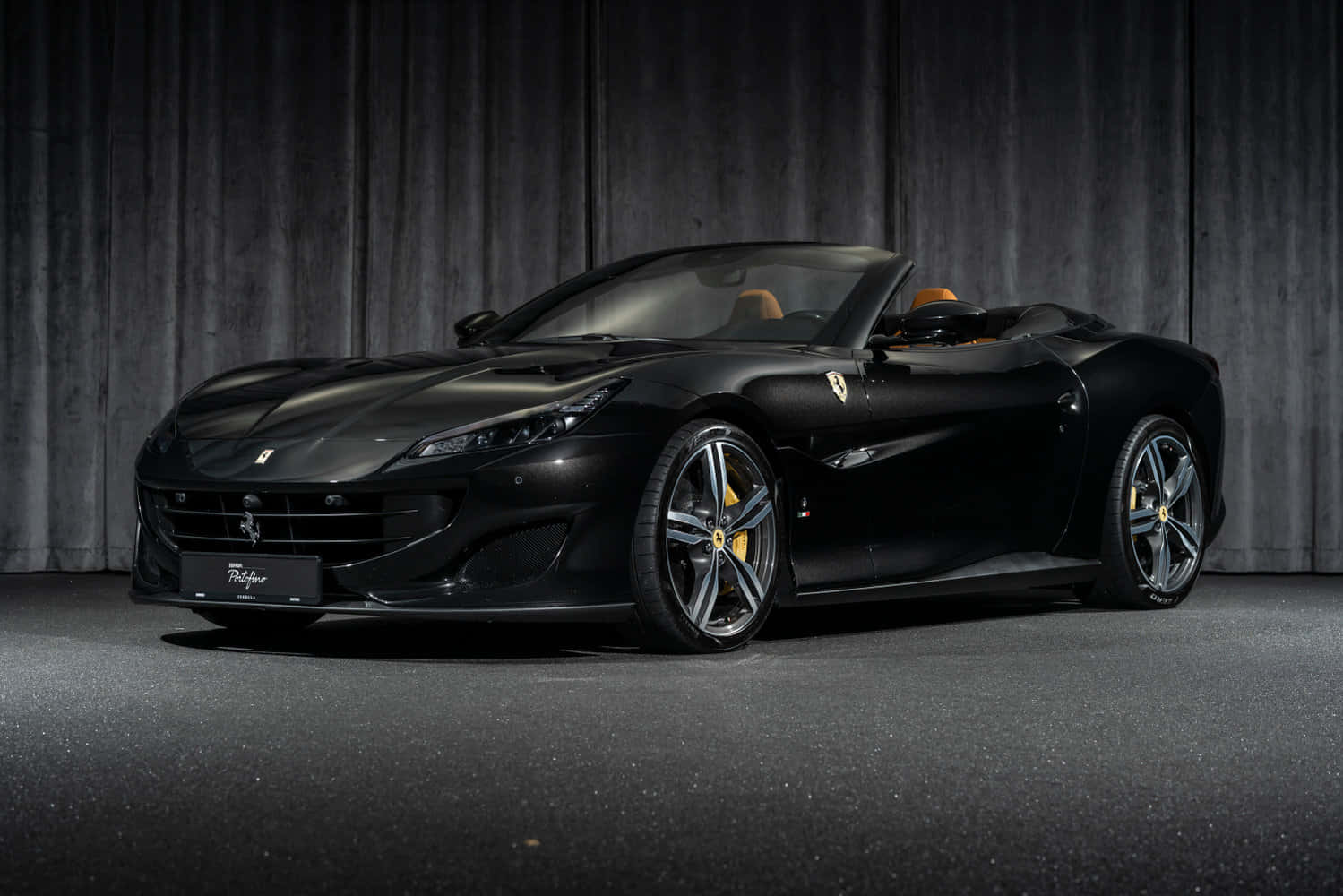 Ferrari Portofino 桌布 壁紙 — 一輛時尚的黑色法拉利 Portofino 敞篷車，配備米色內飾，在工作室燈光下，停在深色木質背景前。