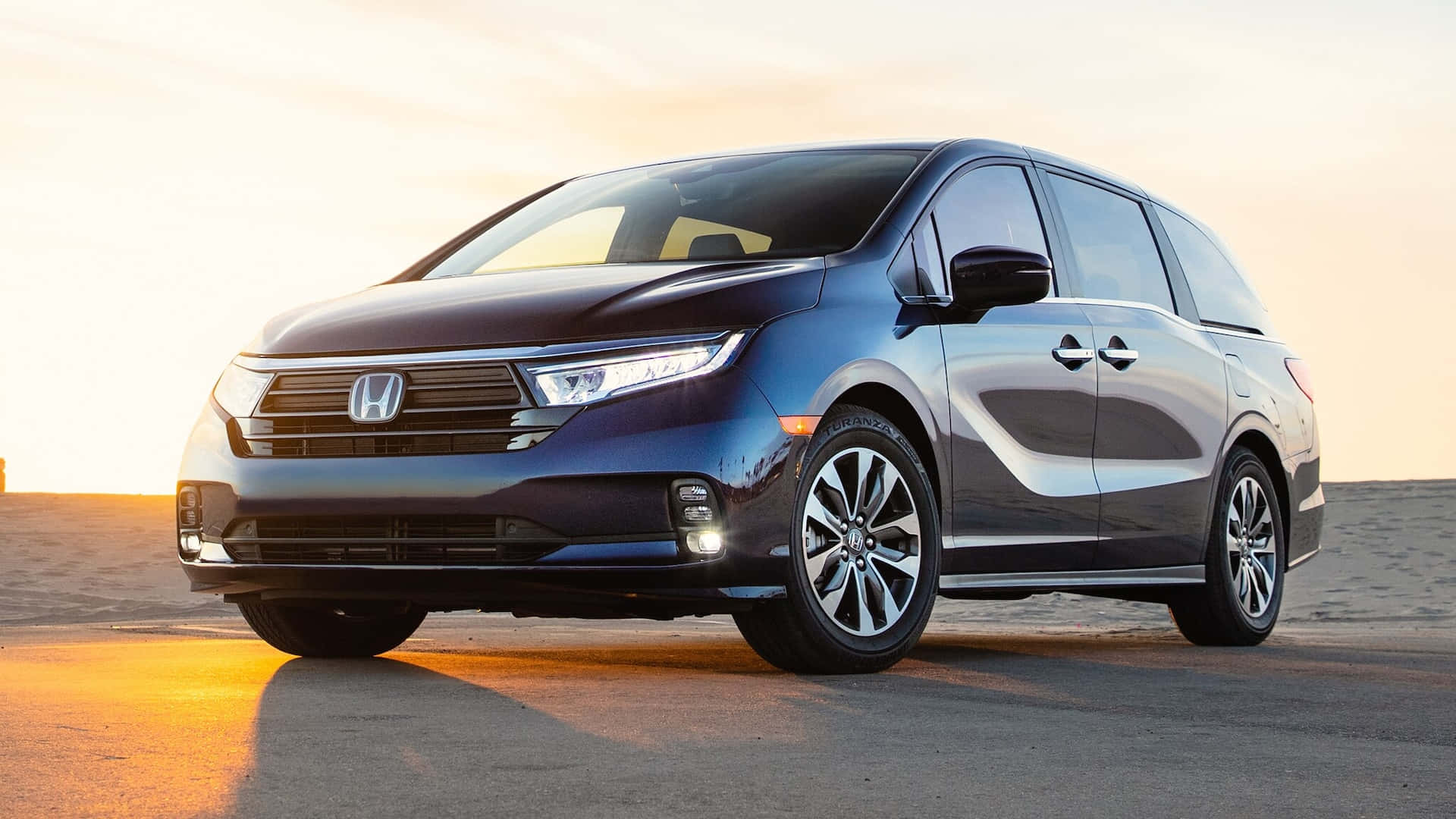 Honda Odyssey 桌布 壁紙 — 一輛時尚的藍色本田小型貨車在沙漠公路上閃耀著金色的日落光芒。