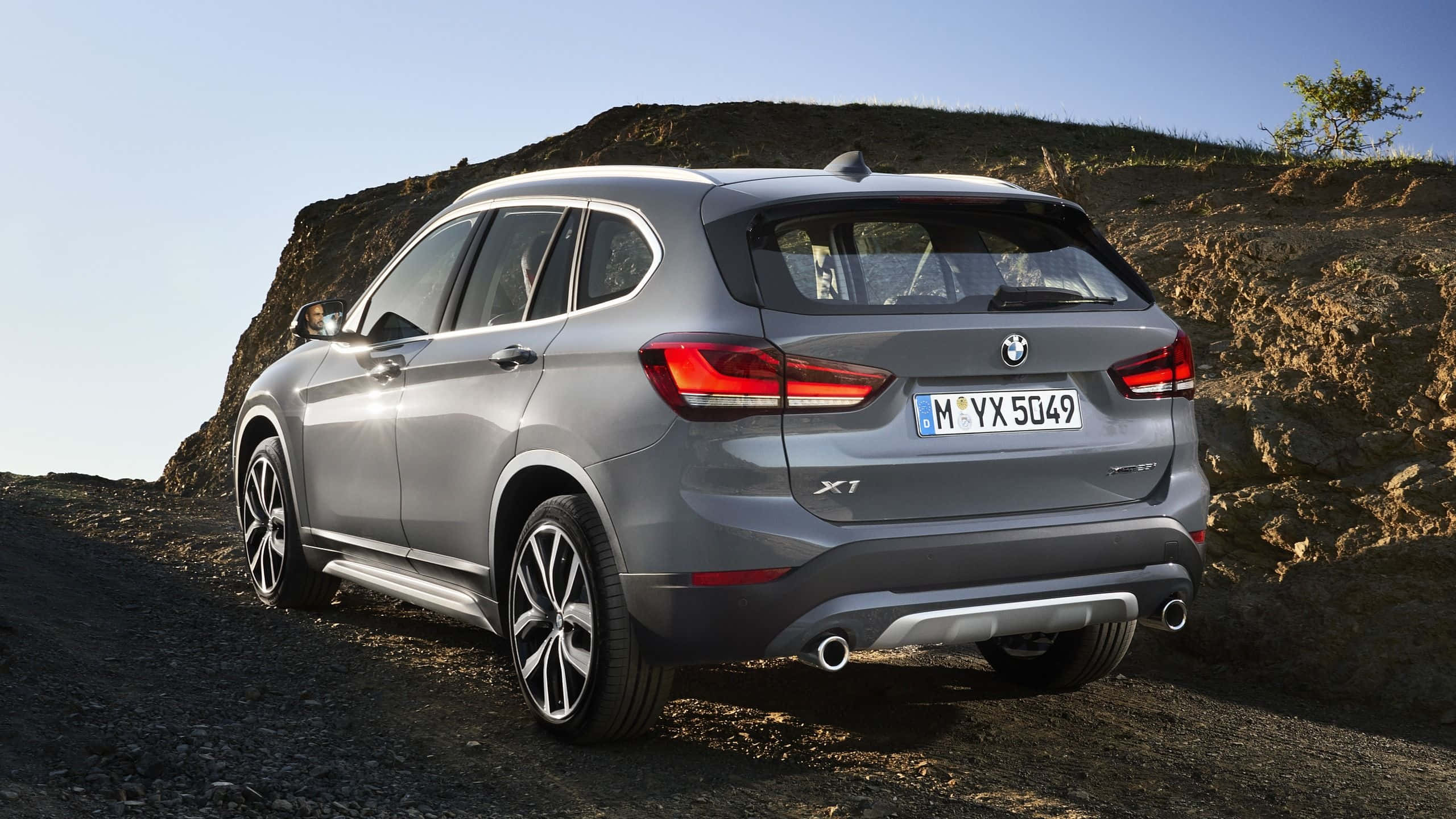 Bmw I8 桌布 壁紙 — 一架時尚的銀色BMW X1 SUV停泊在碎石路上，旁邊是岩石山丘，上方是清澈的藍天。