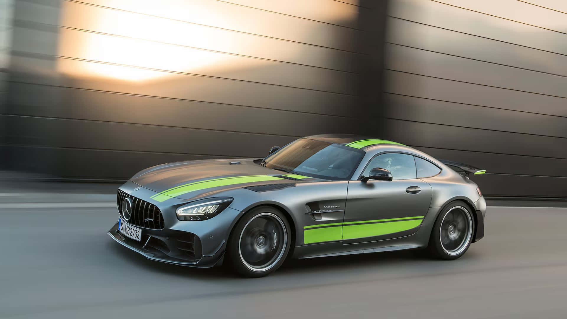  壁紙 — 一輛時尚的銀色 Mercedes-AMG GT R 跑車，帶有螢光綠色條紋，在日落時分飛馳而過現代金屬牆。