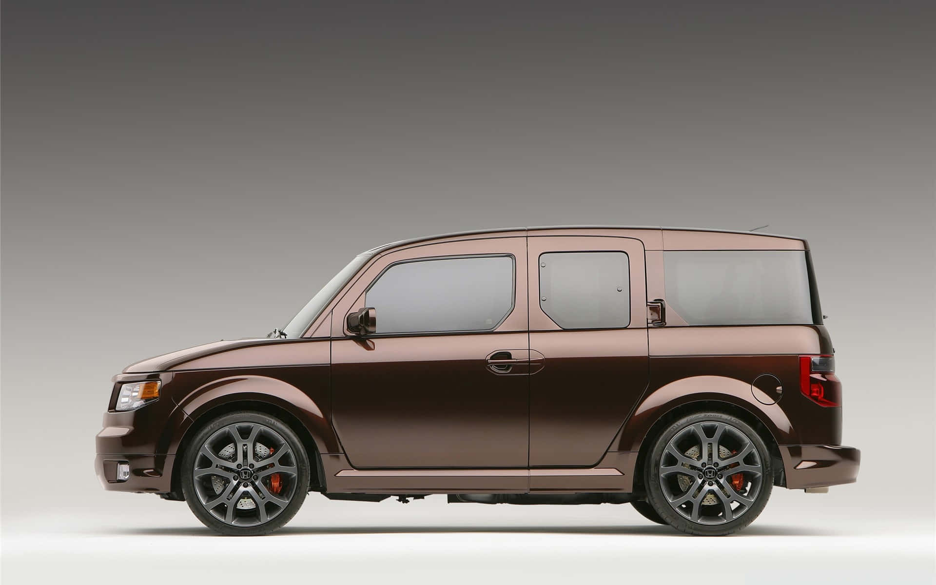 Honda Element 桌布 壁紙 — 一輛時尚的棕色本田Element，配備黑色輪圈和紅色制動卡鉗，在中性工作室背景前以側面展示。