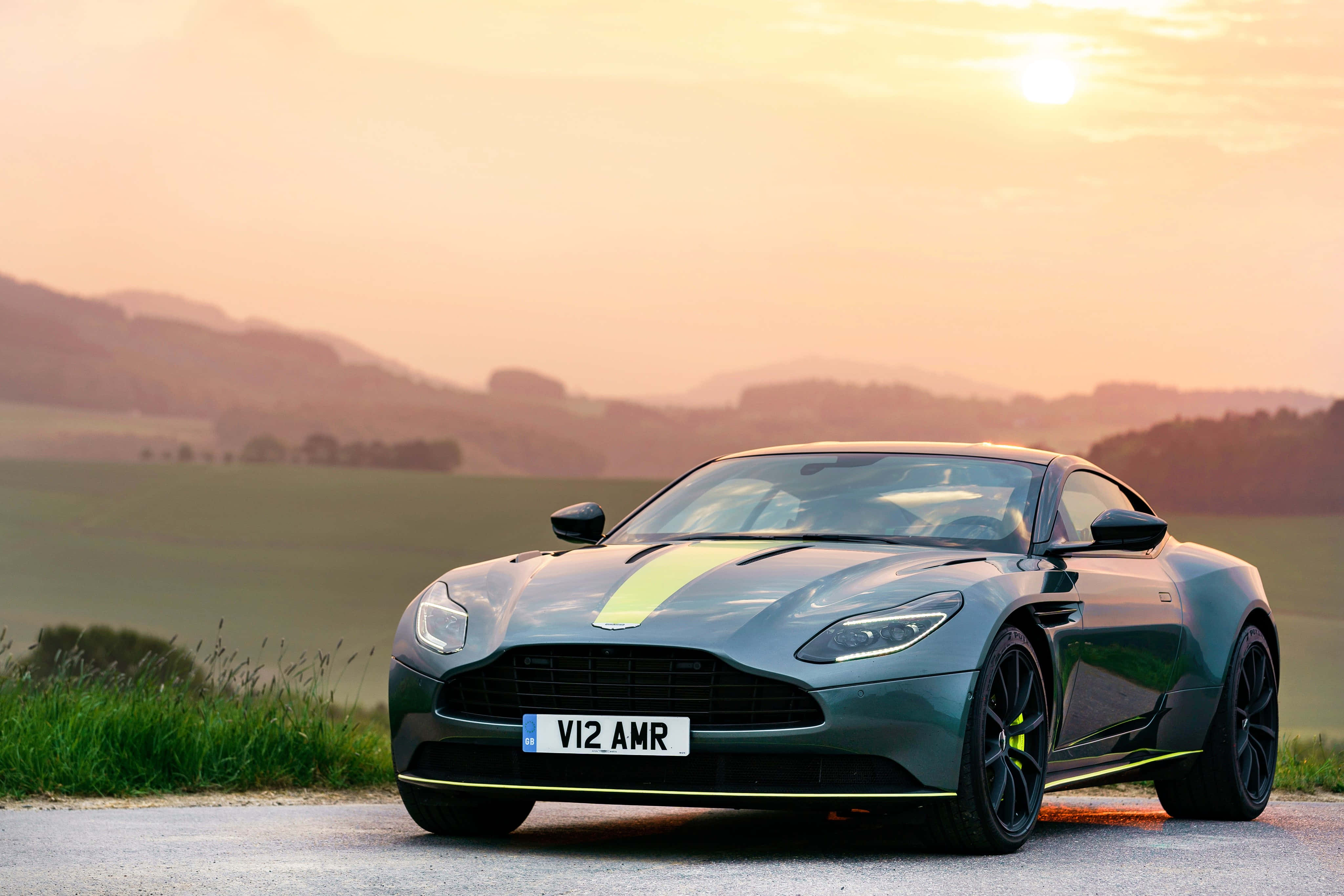 Aston Martin Db11 桌布 壁紙 — 一輛時尚灰色 Aston Martin DB11 AMR 帶有螢光綠色點綴，停泊在金色日落下的鄉村道路上。