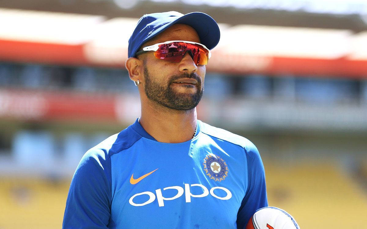 Shikhar Dhawan 戴太陽眼鏡 壁紙 — 一位專注的印度板球運動員穿著藍色訓練裝備，在體育場明亮的日光下拿著一個球。