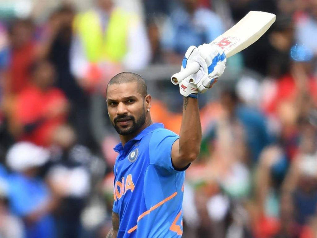 Shikhar Dhawan 持白色球棒 壁紙 — 印度板球運動員在體育場內高舉球棒，在歡呼的人群前慶祝。