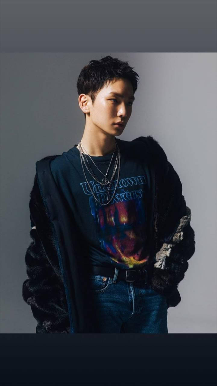 SHINee Key 個人肖像 壁紙 — 一位短黑髮的年輕男士穿著多層次服裝，包括紮染T恤、牛仔褲和黑色毛邊外套，背景是純灰色攝影棚。