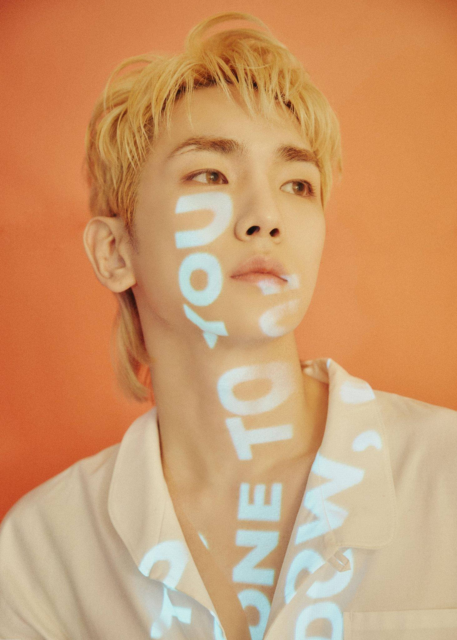 Shinee Key Orange 壁紙 — 一位金髮年輕男子向上凝視，發光的白色文字投射在他的臉上，背景是溫暖的橙色。
