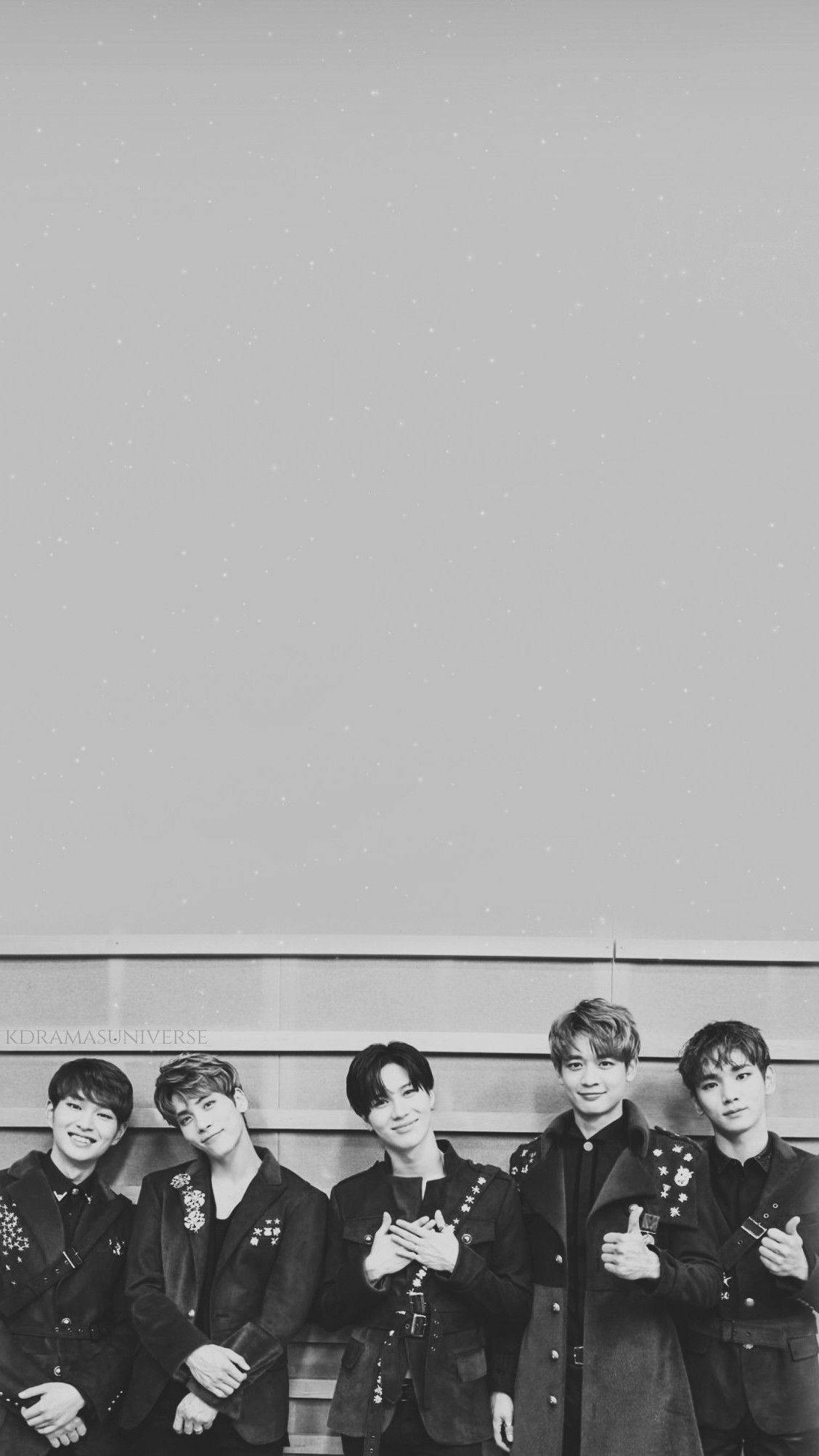SHINee 黑白風 壁紙 — 五位年輕男士身穿時尚黑色外套，在帶有細微紋理的簡約灰色牆壁前自信擺姿勢。