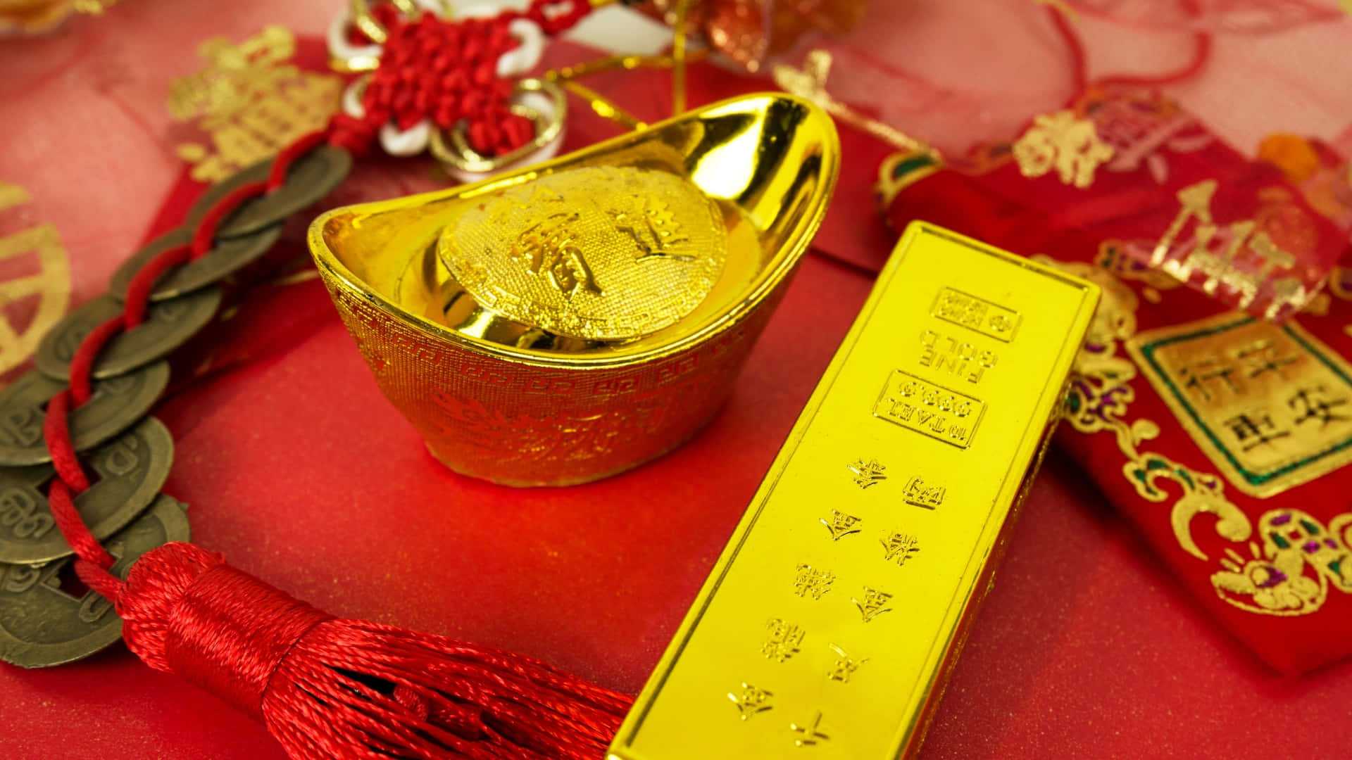  壁紙 — 閃亮的金錠和金條放在紅色布料上，旁邊有中國硬幣和節日紅色流蘇。