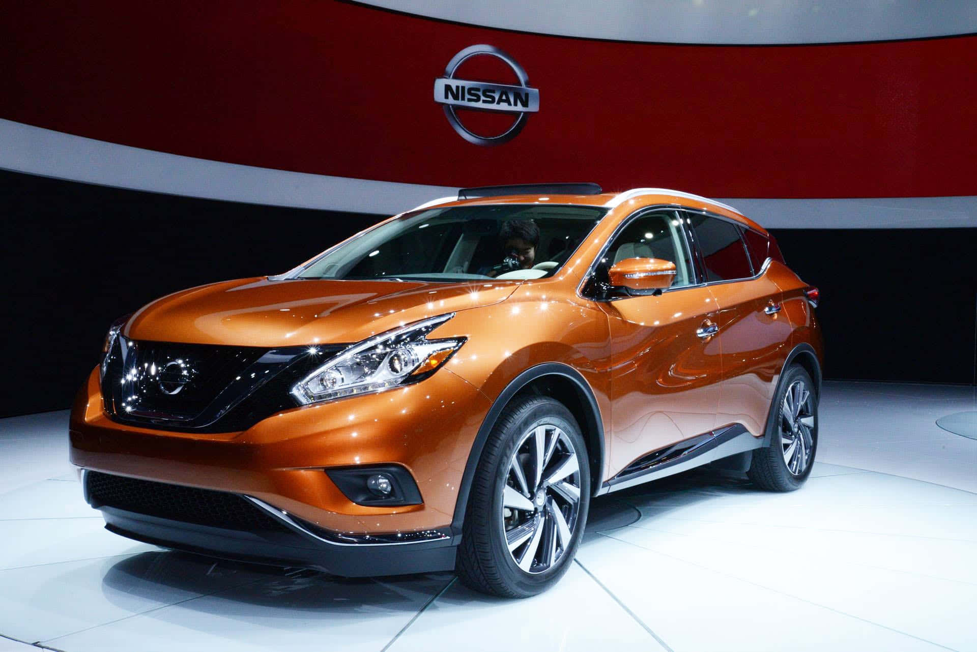 Nissan Murano 桌布 壁紙 — 一輛閃亮的橙色日產Murano SUV在白色平台上，在明亮的燈光下，於紅色和白色弧形背景的車展中展示。