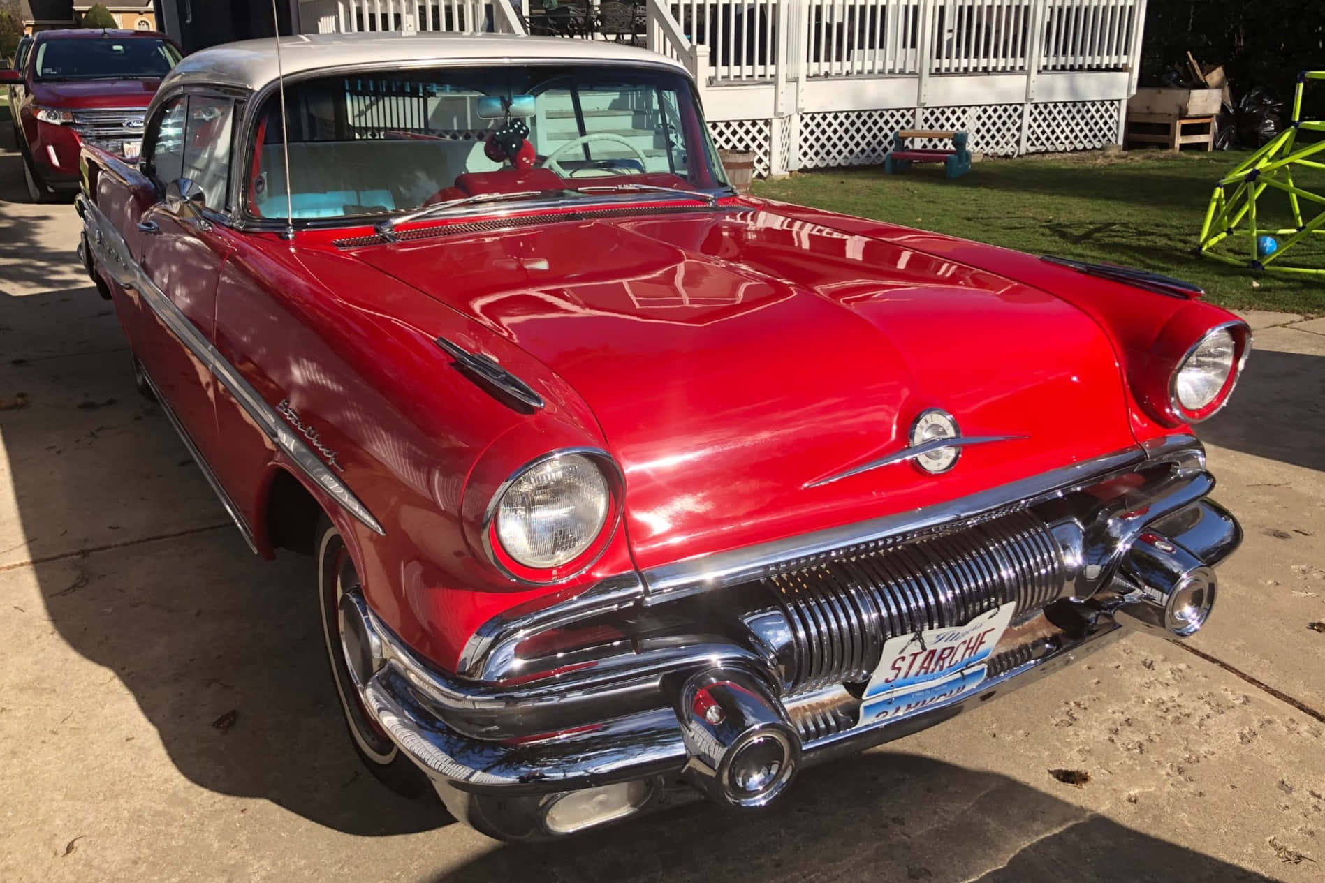 Pontiac Star Chief 桌布 壁紙 — 一輛閃亮的紅色1950年代雪佛蘭，帶有鍍鉻細節，停在白色圍欄附近的陽光車道上。