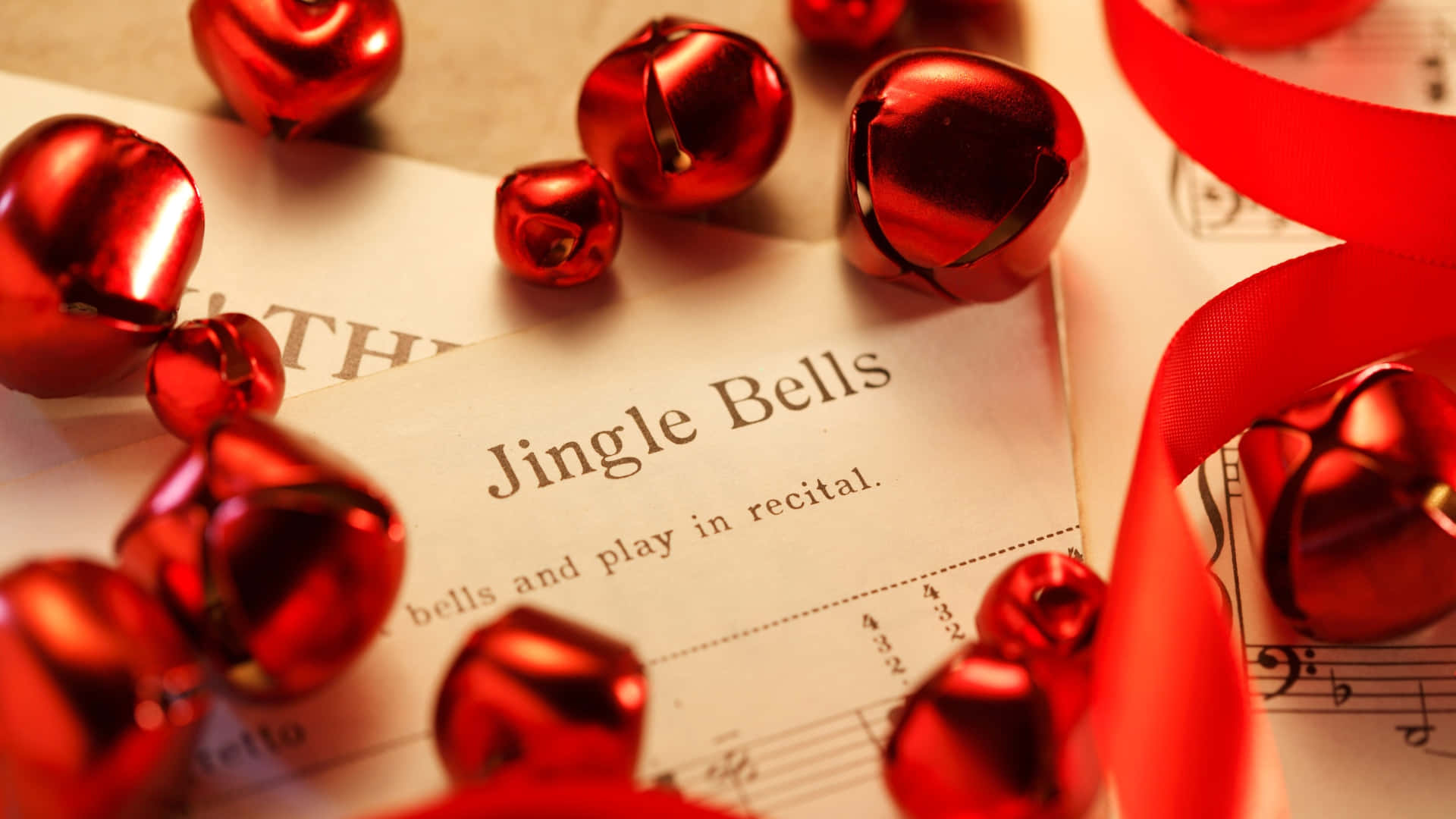  壁紙 — 閃亮的紅色聖誕鈴鐺和絲帶點綴著復古的《Jingle Bells》樂譜，在溫暖的節日燈光下。