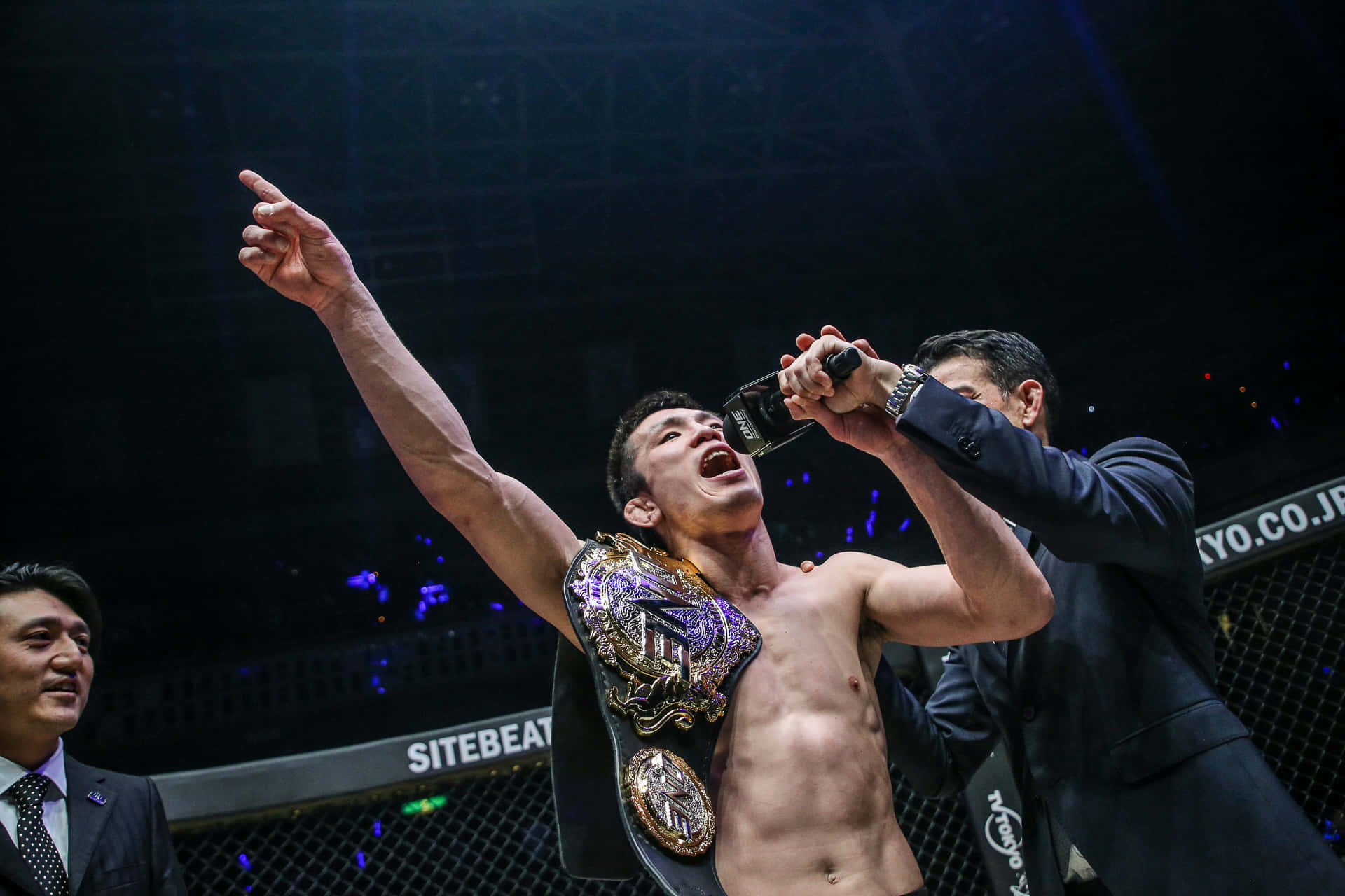 Shinya Aoki 在日本慶祝勝利 壁紙 — 一位勝利的MMA拳手在八角籠中慶祝，被噴灑香檳，同時戴著冠軍腰帶。