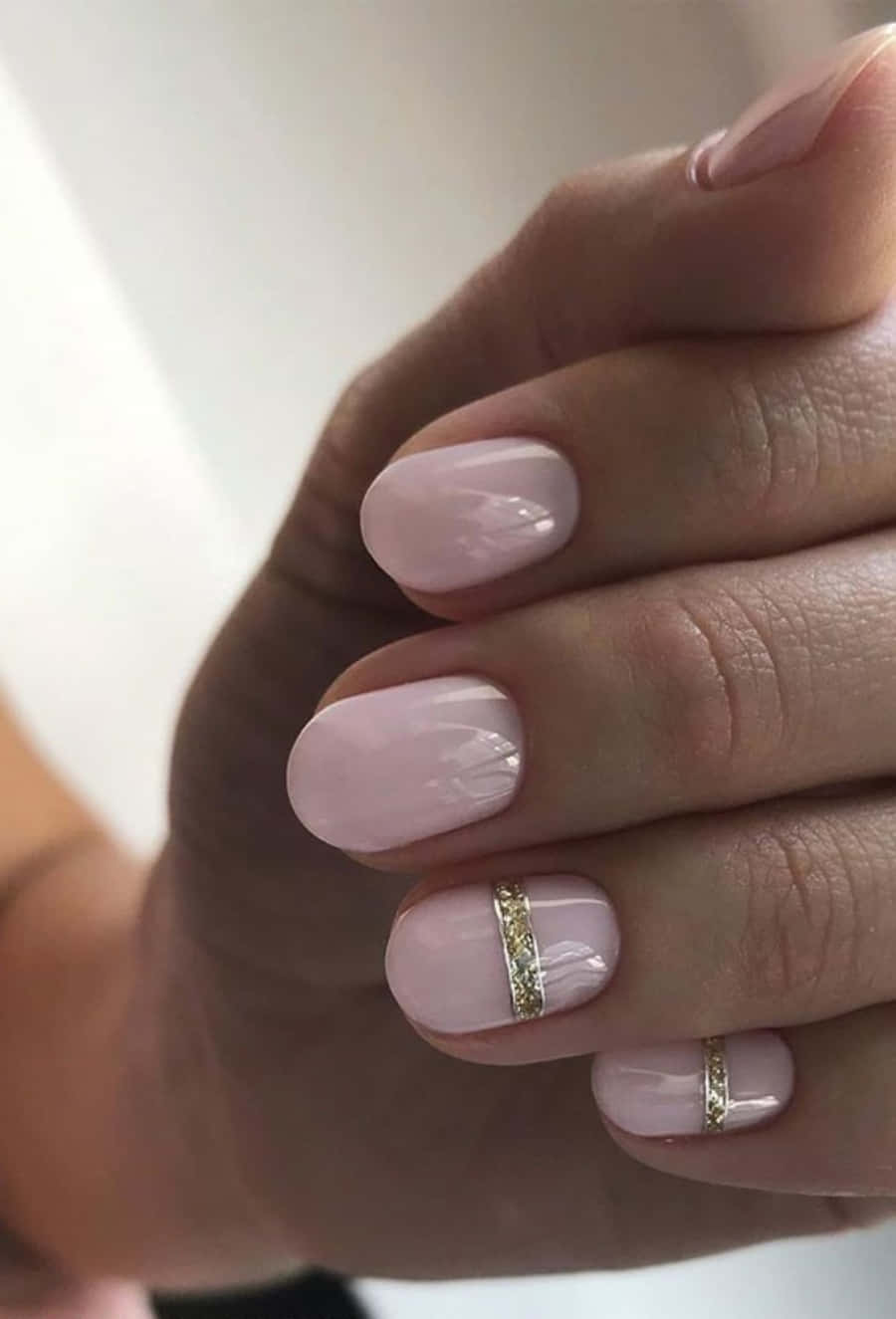 Pink Nail Art 桌布 壁紙 — 手部特寫，指甲呈柔和粉紅色，兩隻手指上有精緻的金色閃粉條紋。