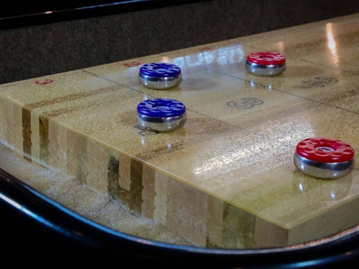 Shuffleboard 桌上的藍紅球 壁紙 — 紅色和藍色冰壺石的特寫，放置在拋光木製冰壺道上，可見木紋和標記。