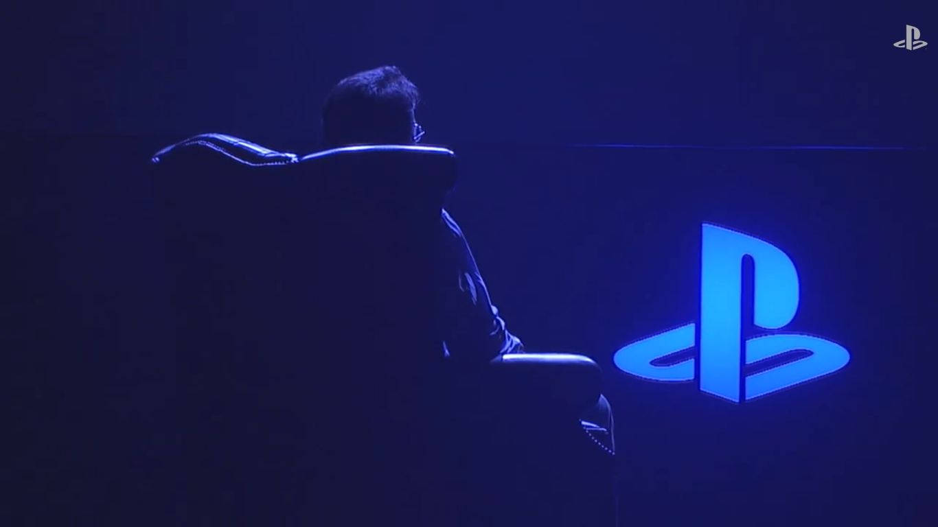 索尼互動娛樂全球工作室總裁Shuhei Yoshida於Gamescom現場體驗最新PS4遊戲 壁紙 — 一個人坐在電競椅上，面向黑暗房間中發光的藍色PlayStation標誌。